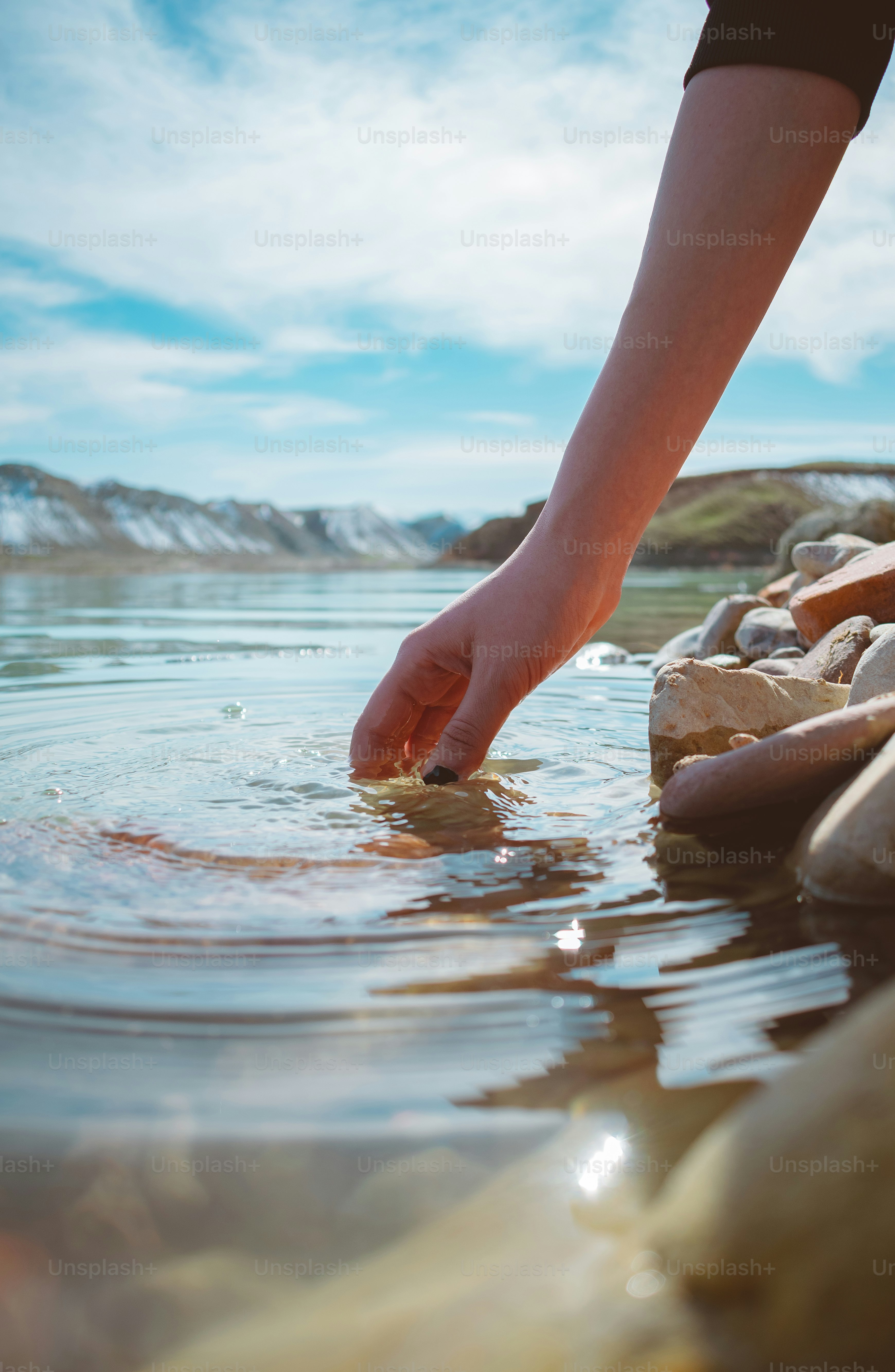 A person reaching for a rock in the water