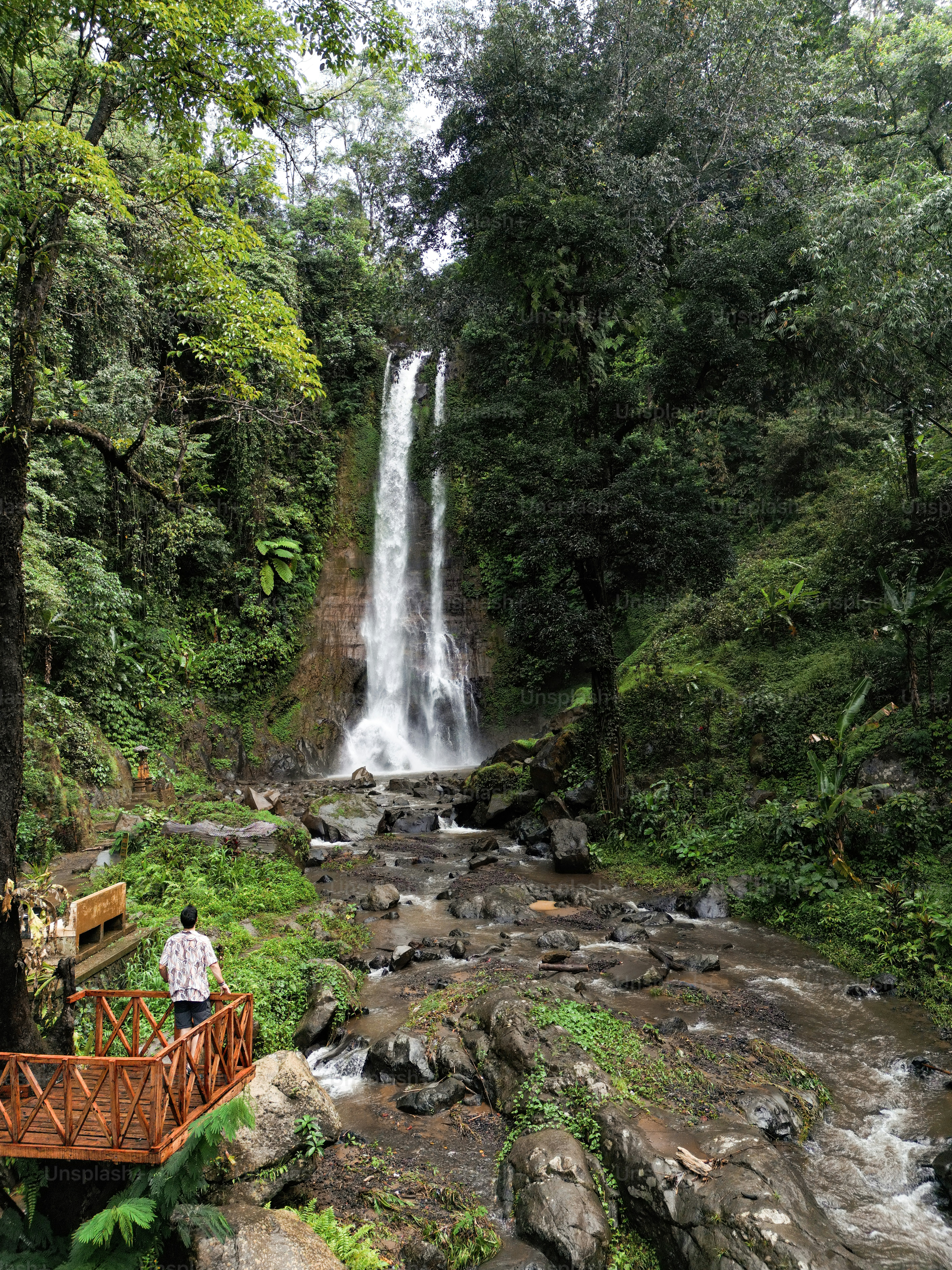 A man standing on a bridge next to a waterfall