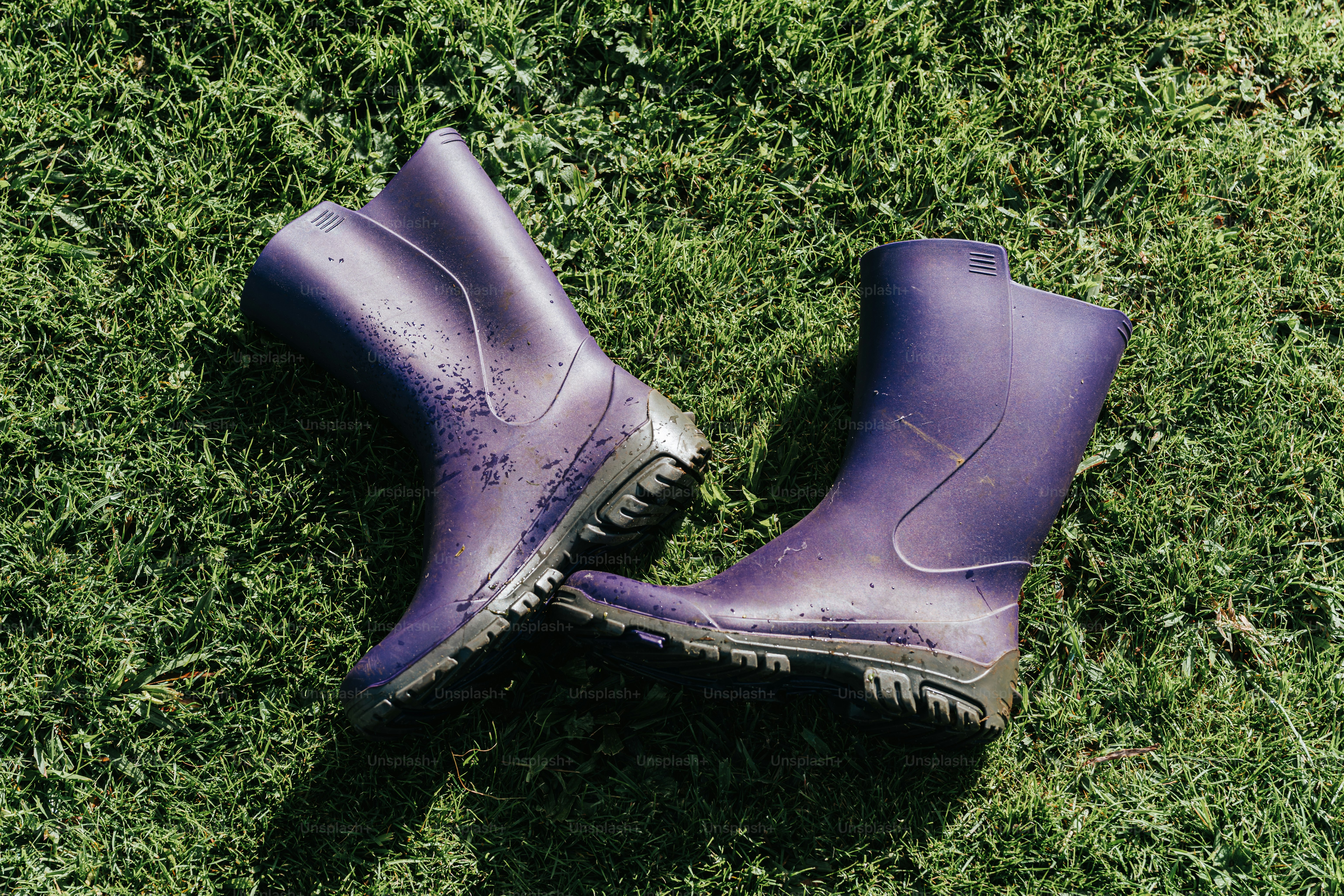 A pair of purple boots laying on top of a green field