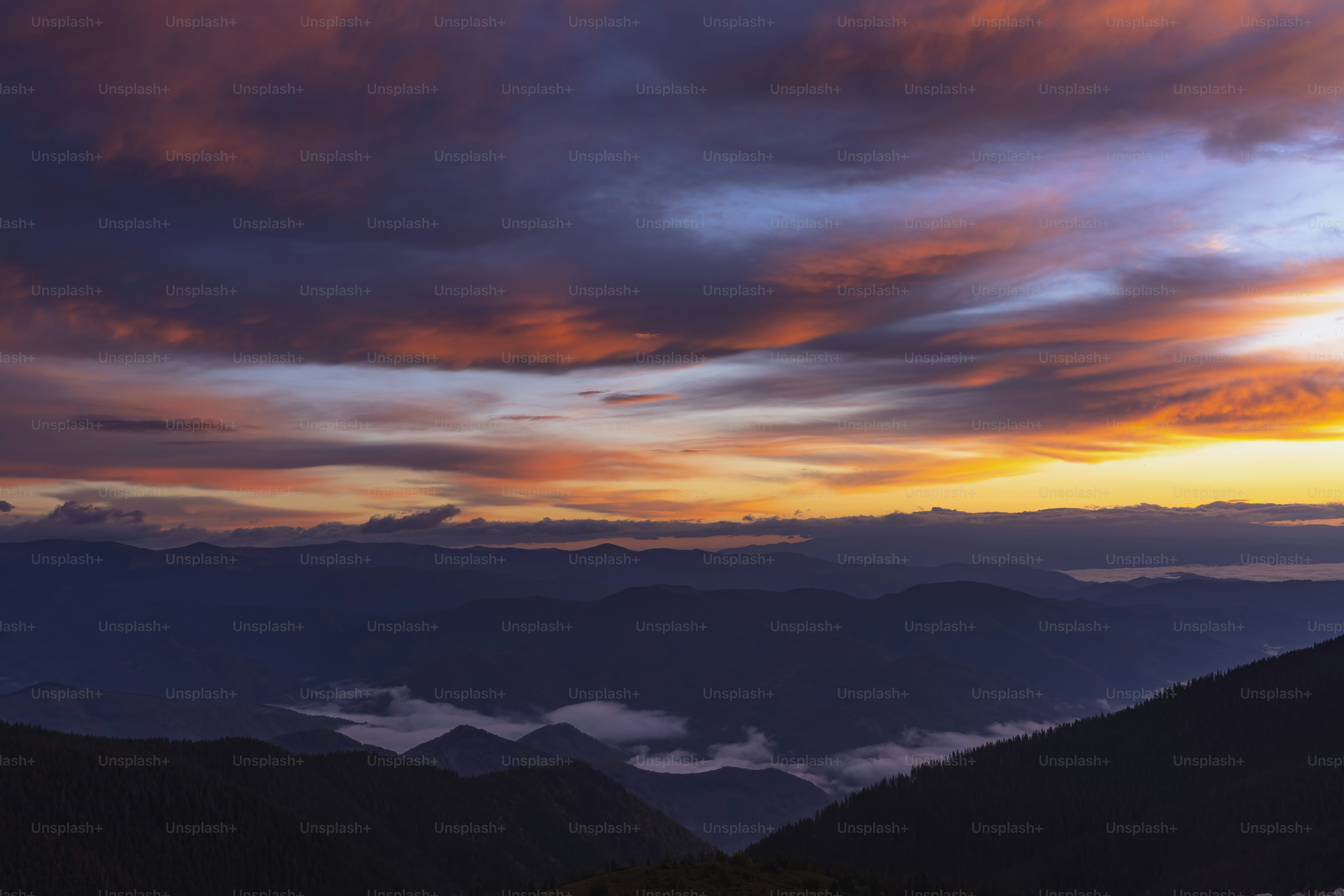 A view of a sunset with clouds and mountains in the background