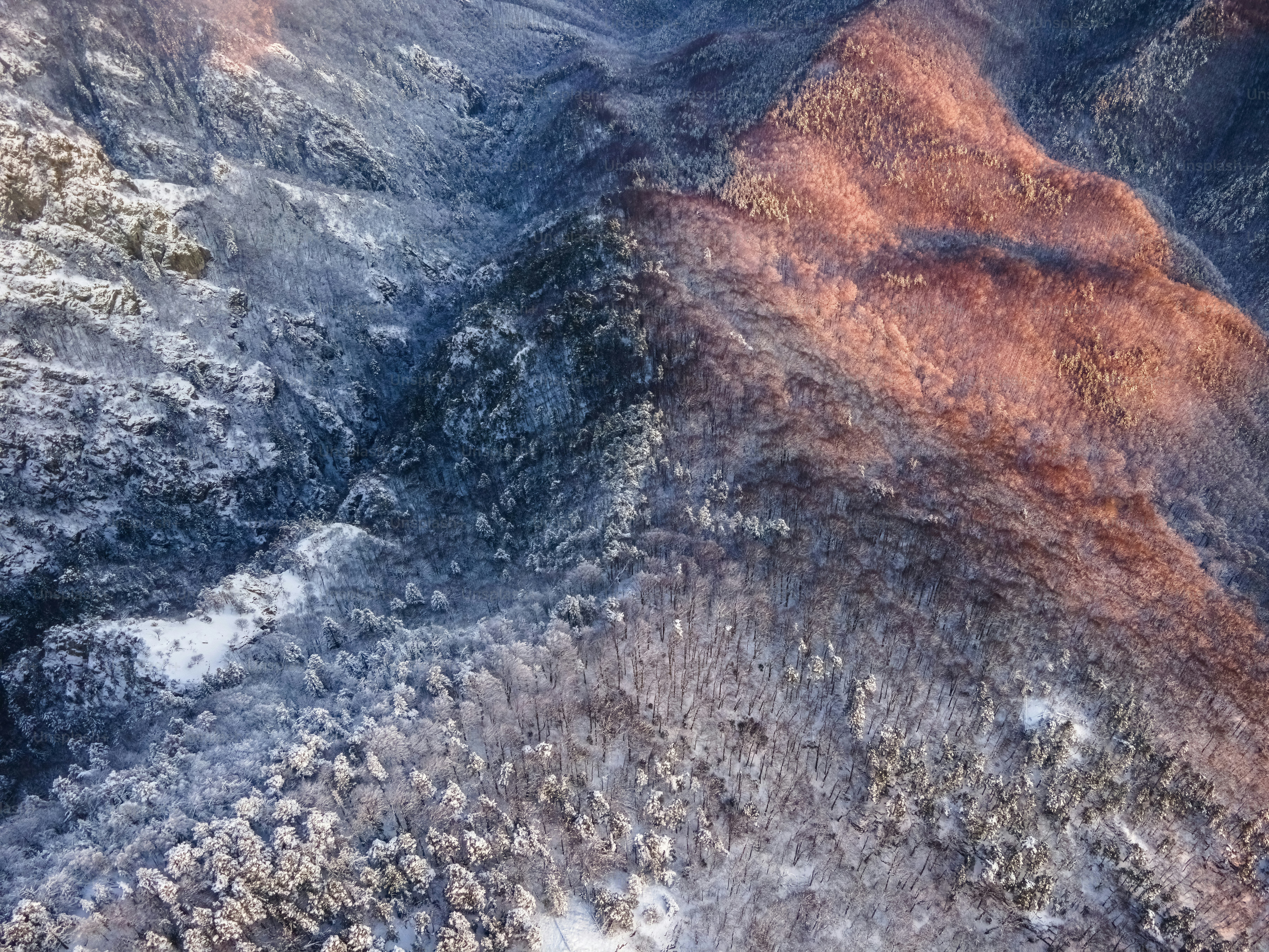 An aerial view of a mountain range with snow on the ground