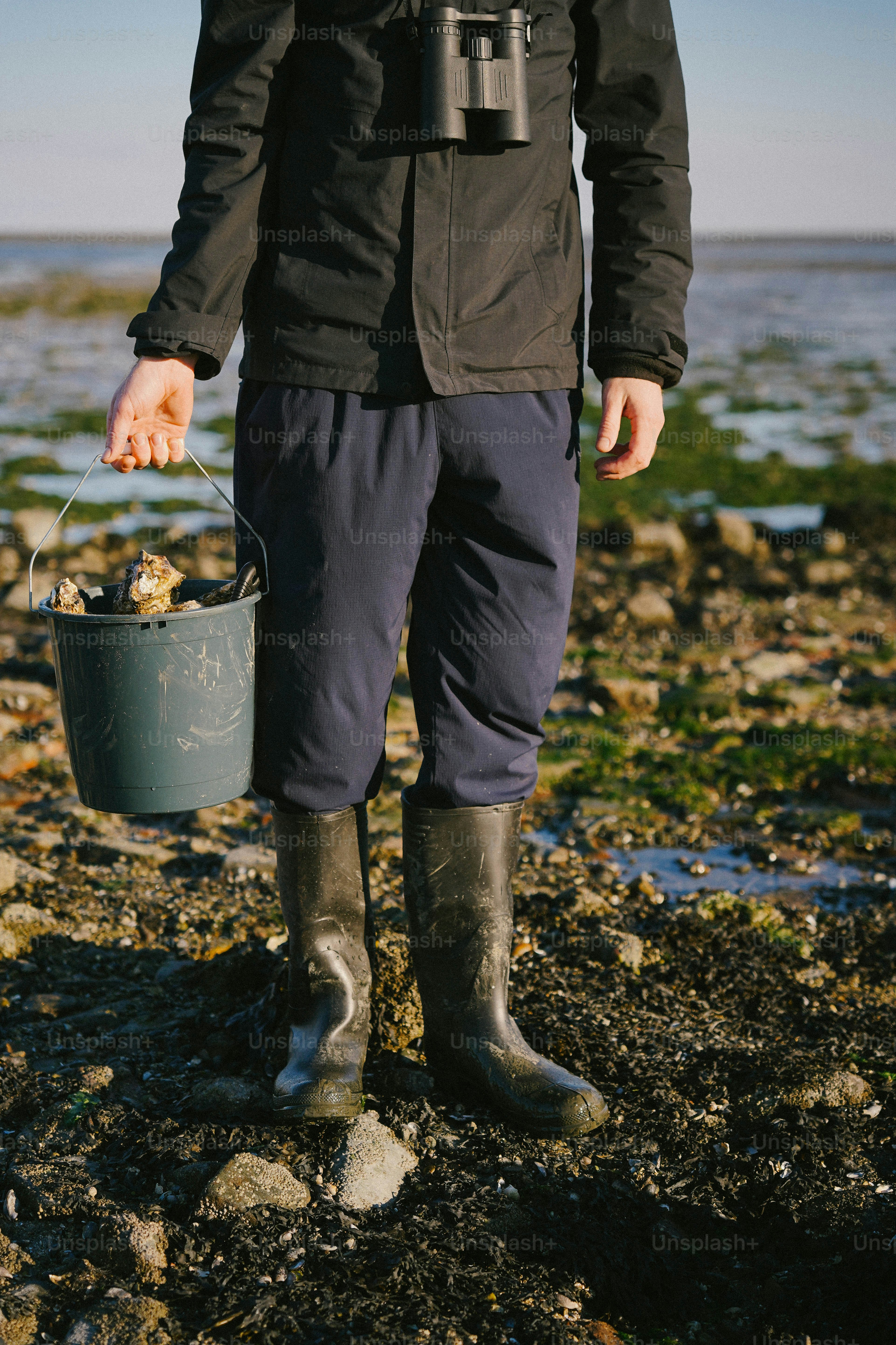 A man standing on a rocky beach holding a bucket
