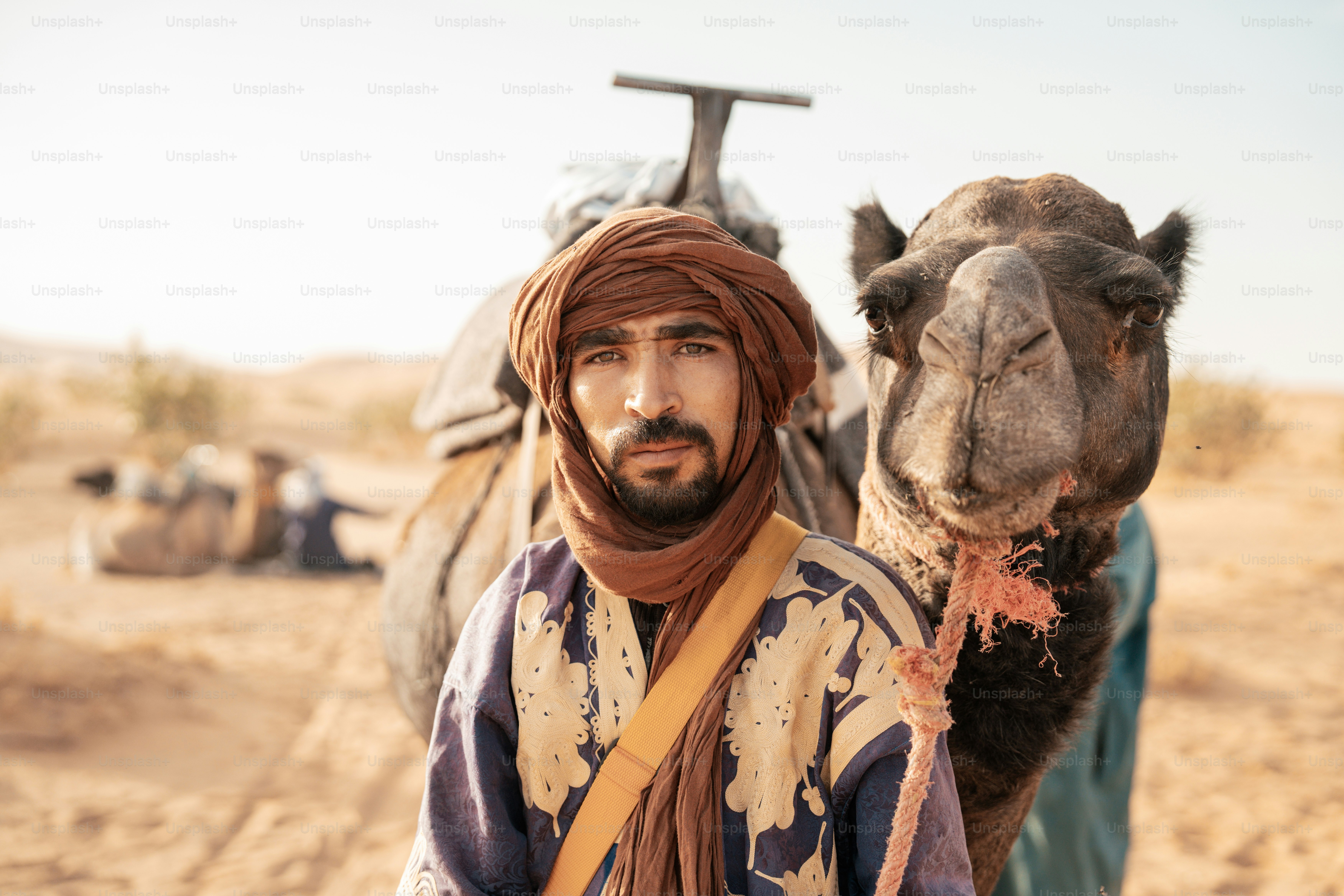 A man in a turban standing next to a camel