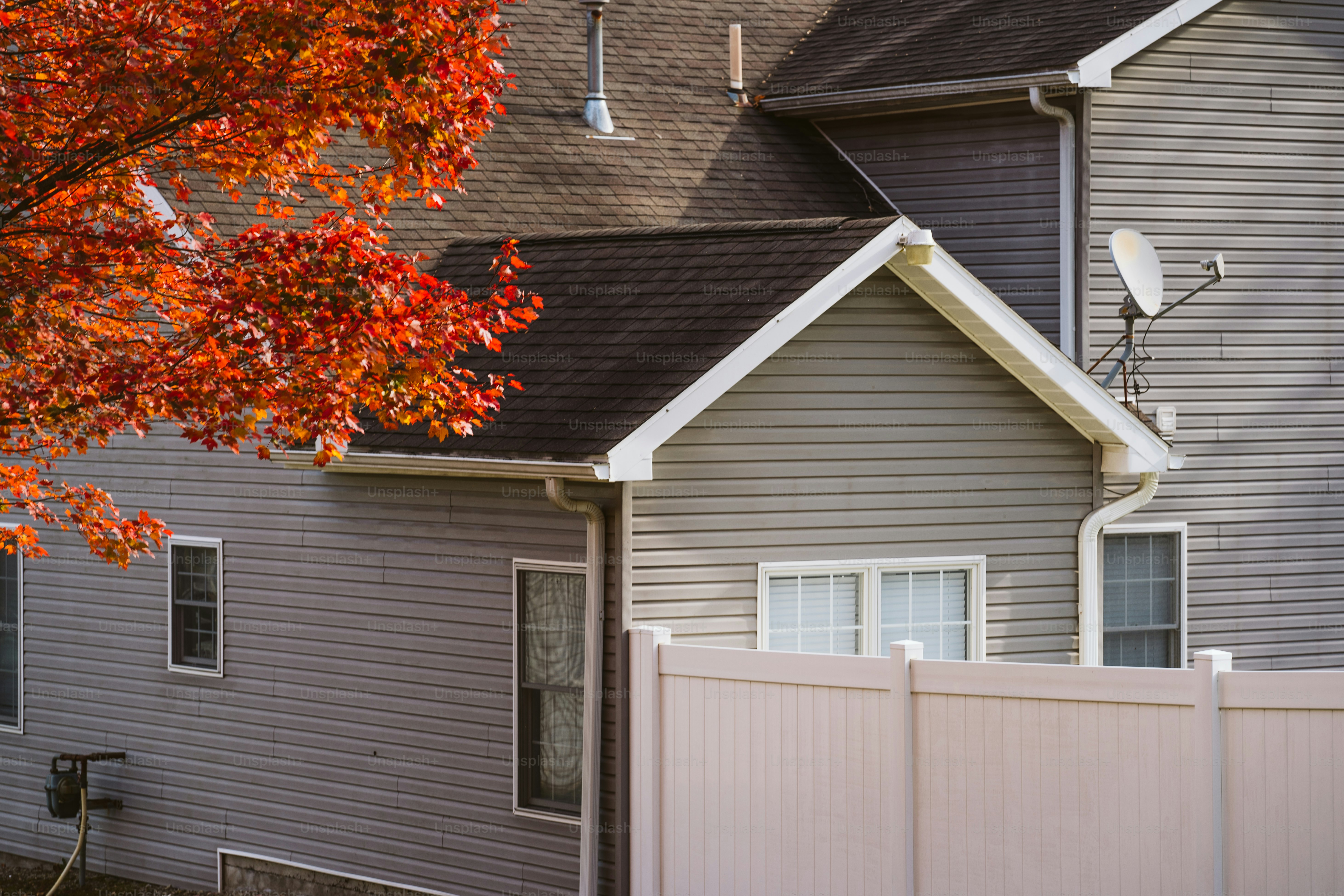 Una casa con una valla blanca y un árbol rojo delante