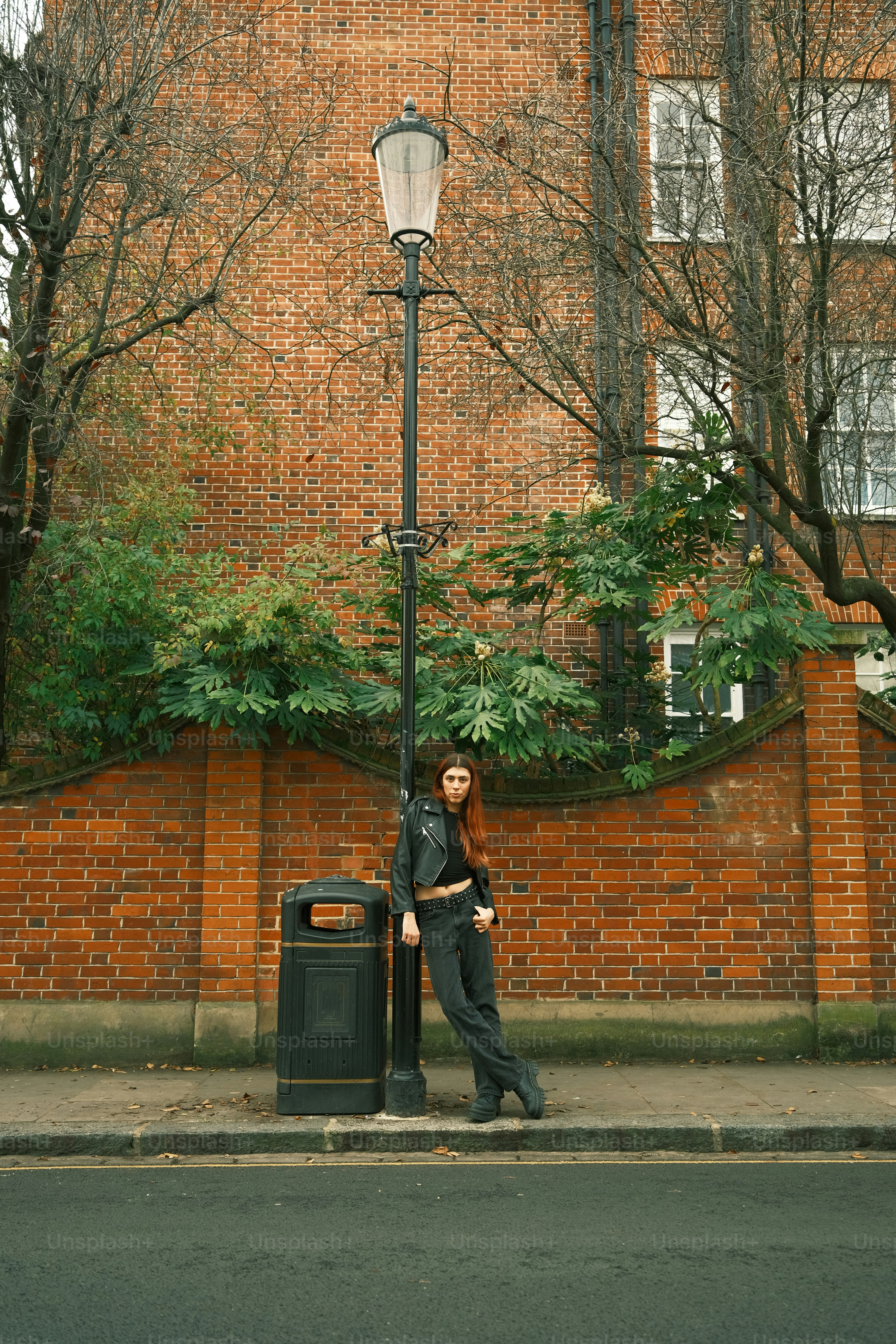 レンガ造りの建物の前で街灯柱にもたれかかっている女性