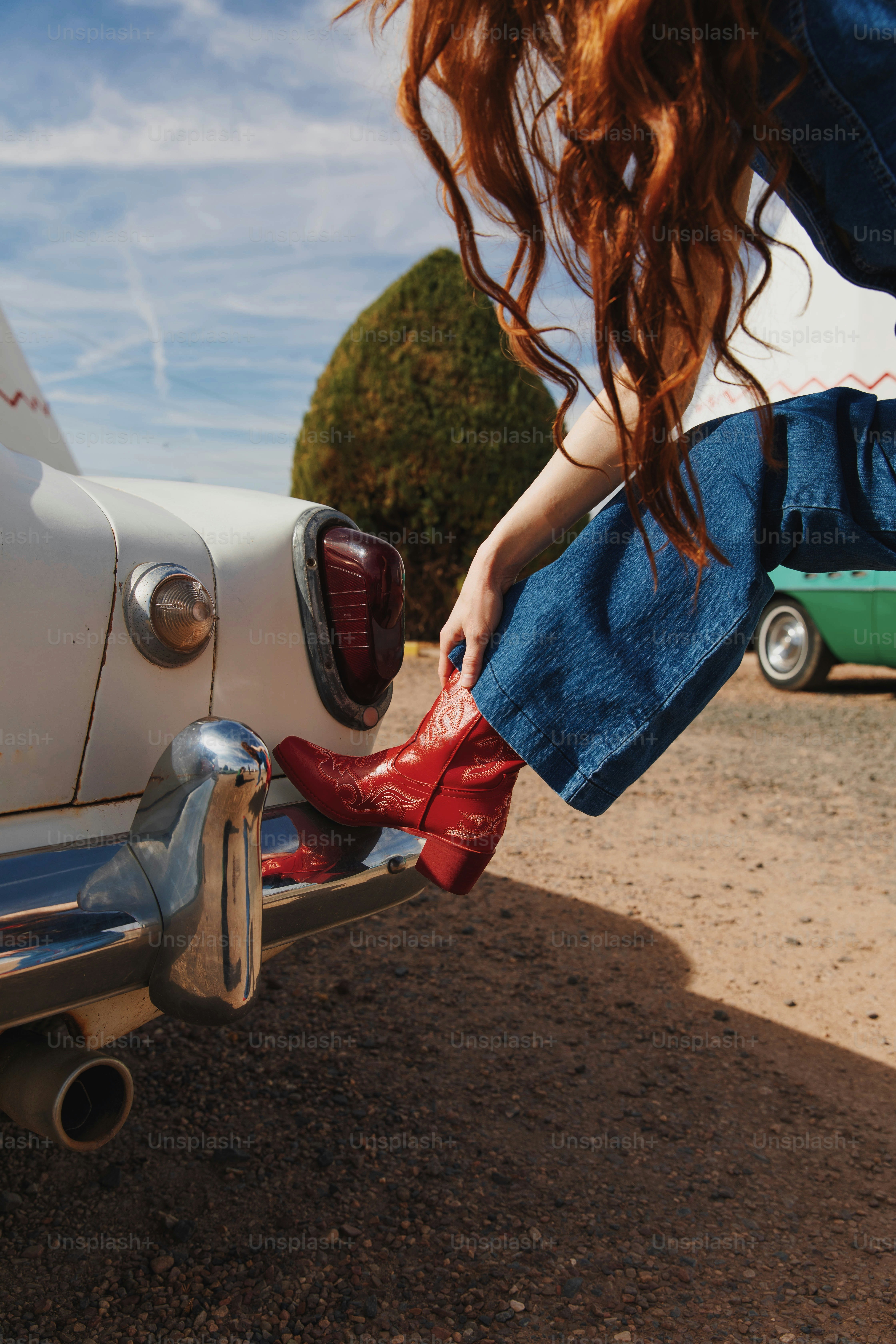 A woman with red boots is leaning on a car