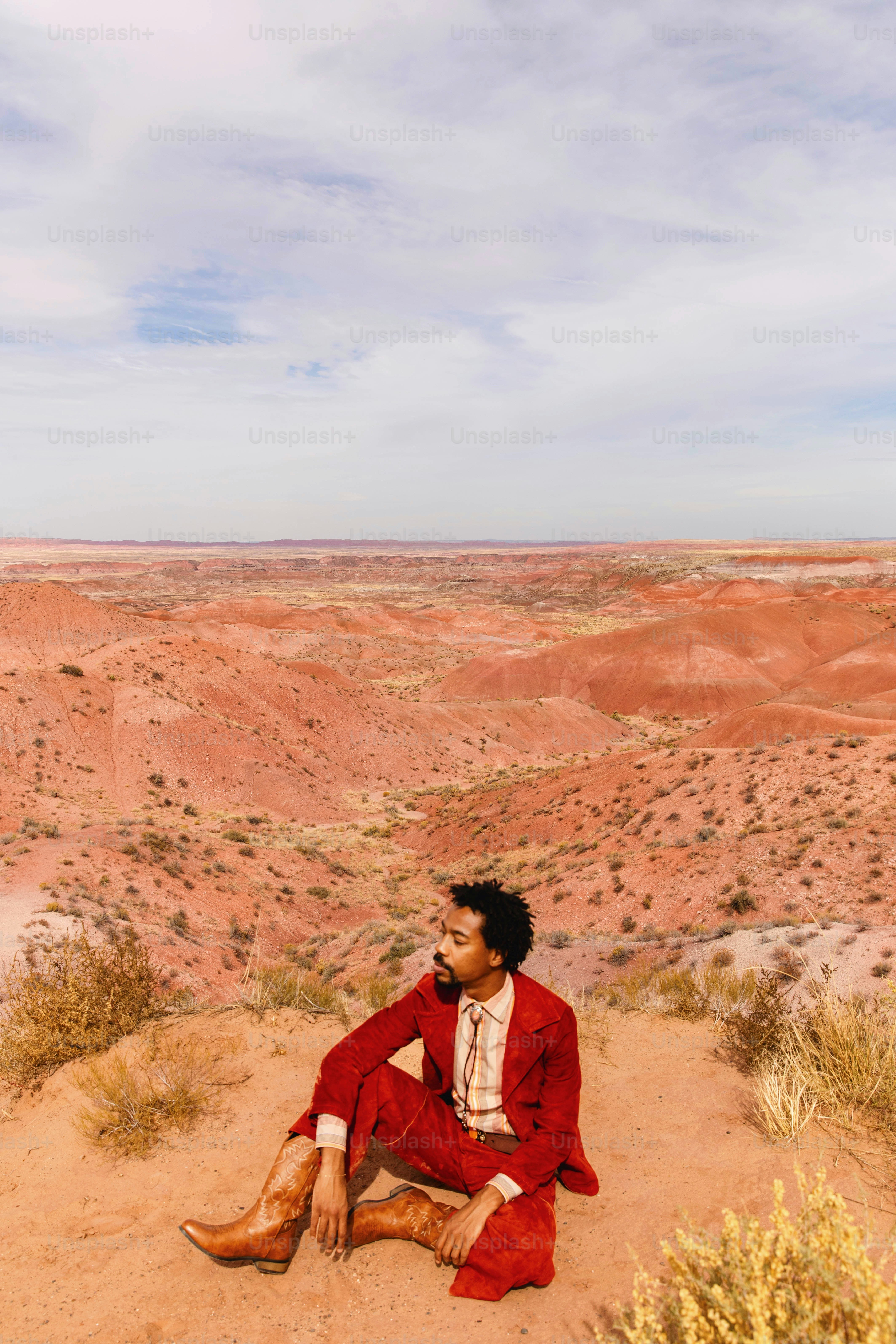A man in a red suit sitting on top of a hill photo – Red suit Image on ...