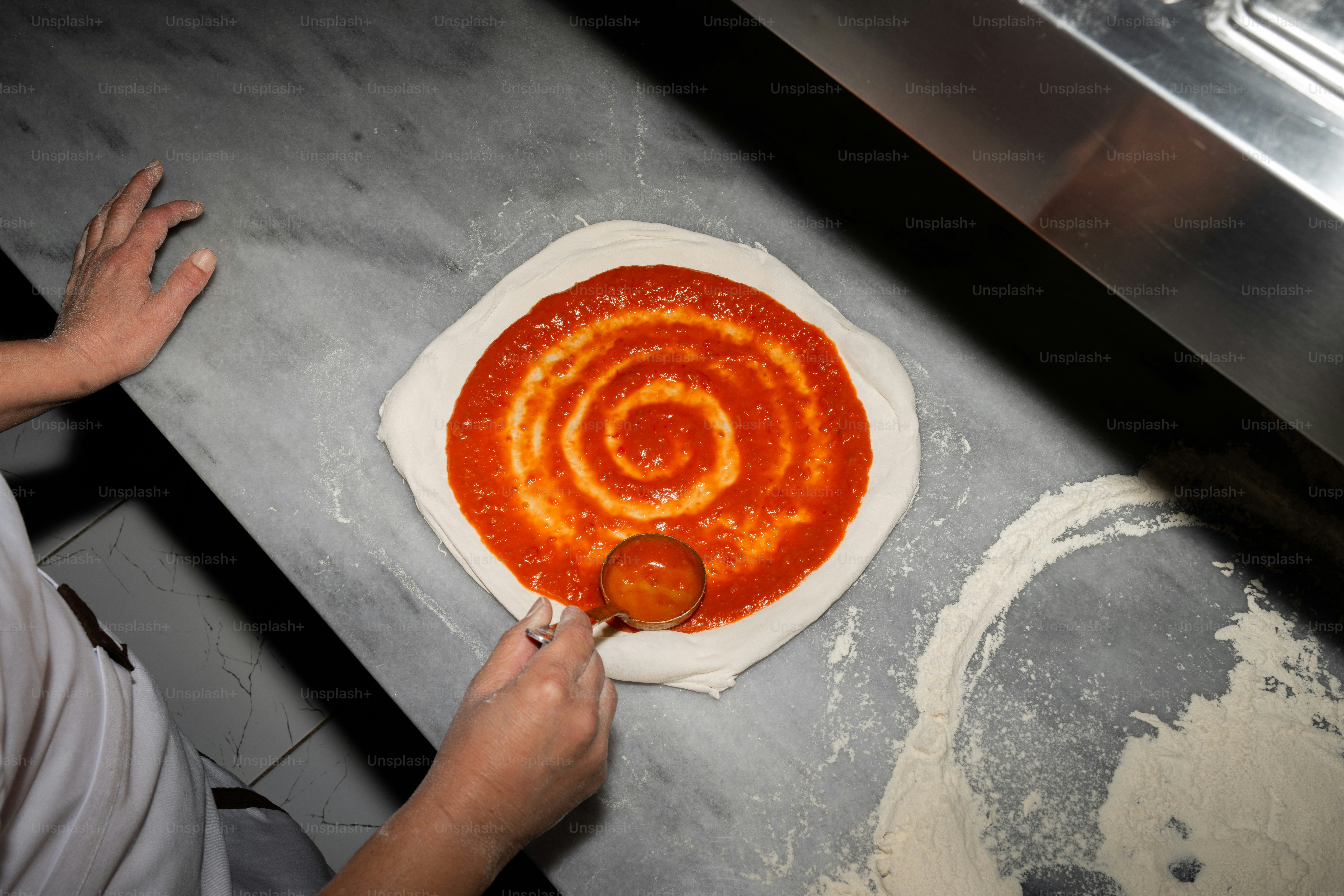 A person making a pizza with sauce on it