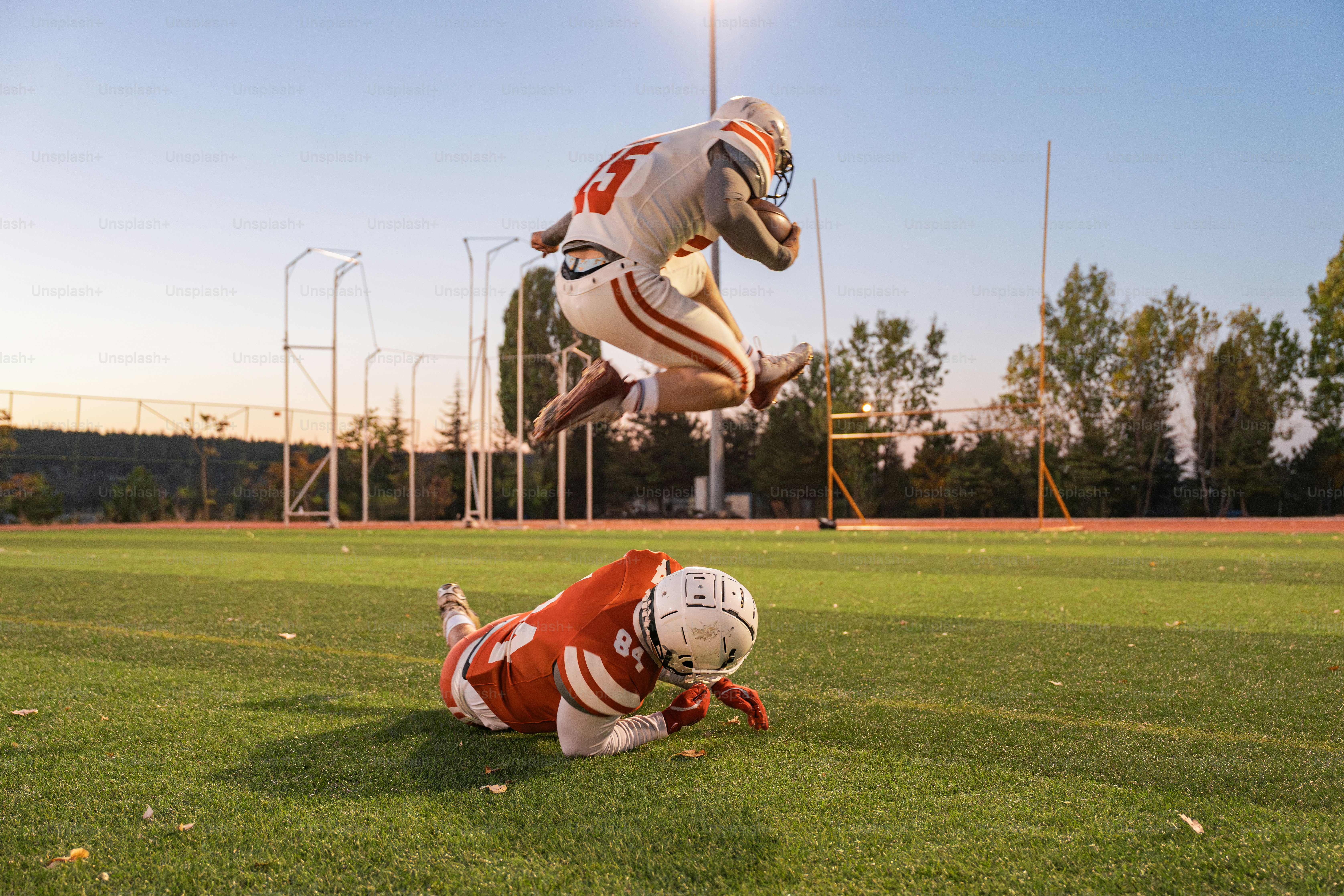 A football player jumping over another player on a field