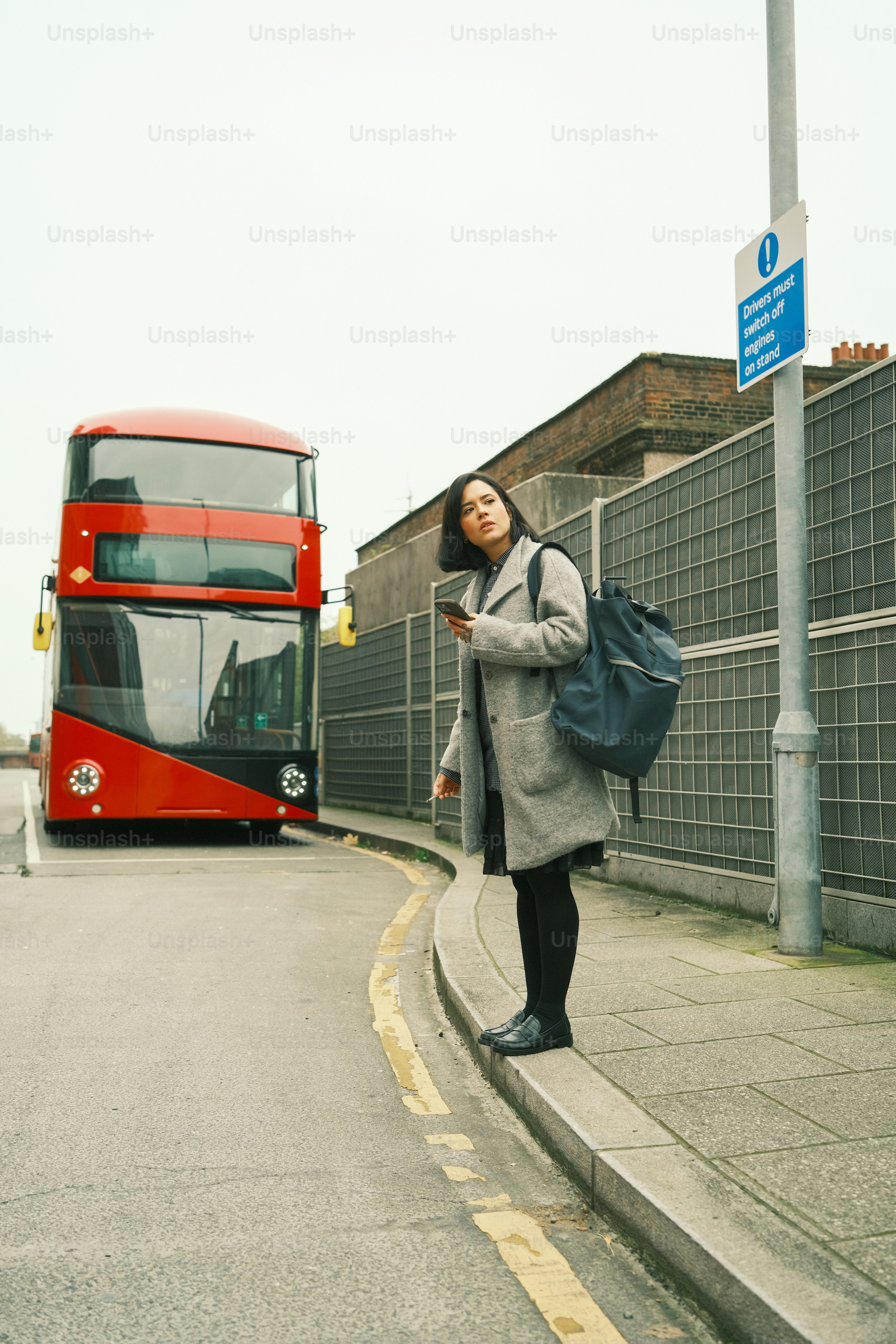 A woman standing on the side of a road next to a red double decker bus