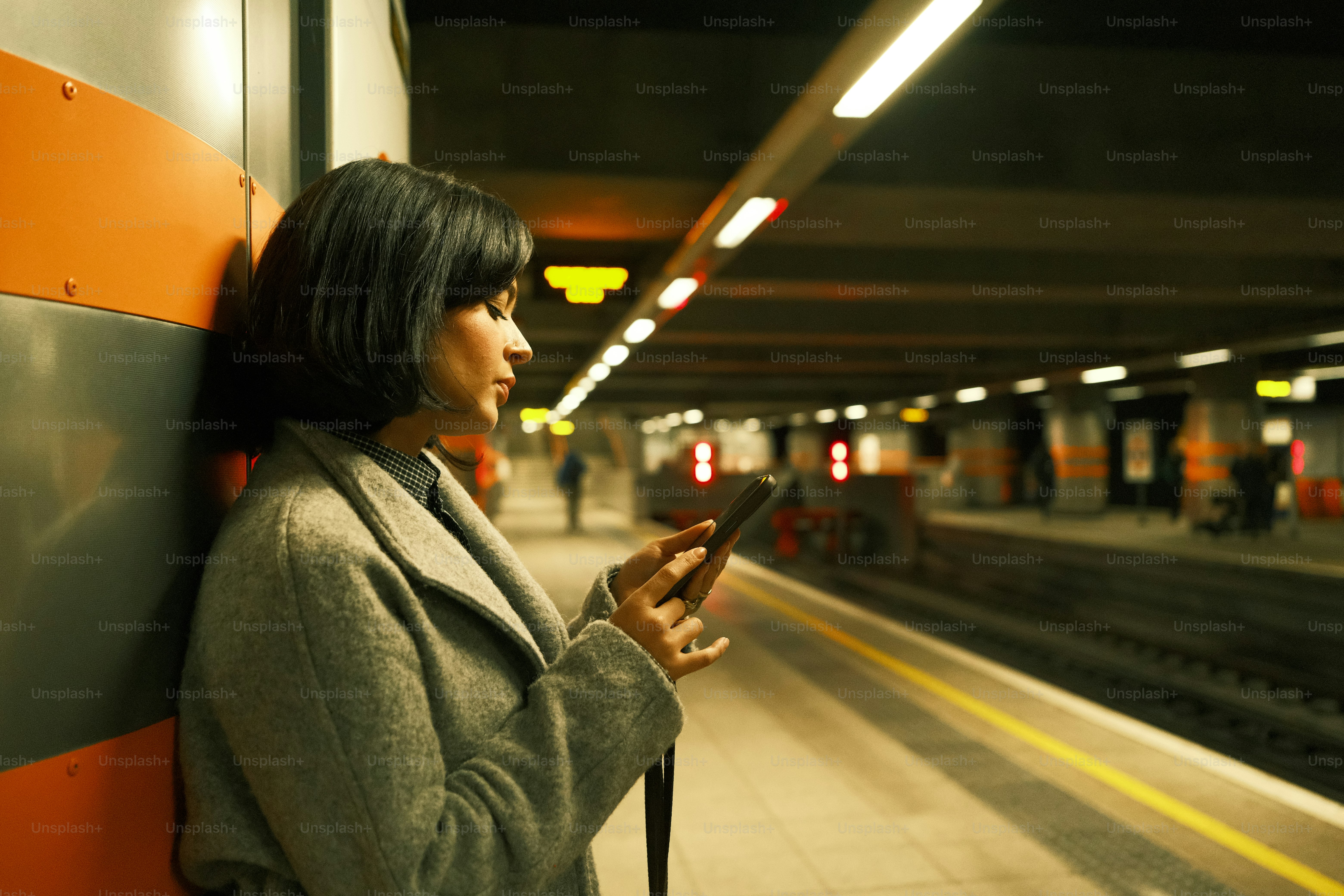 A woman leaning against a wall while looking at her cell phone
