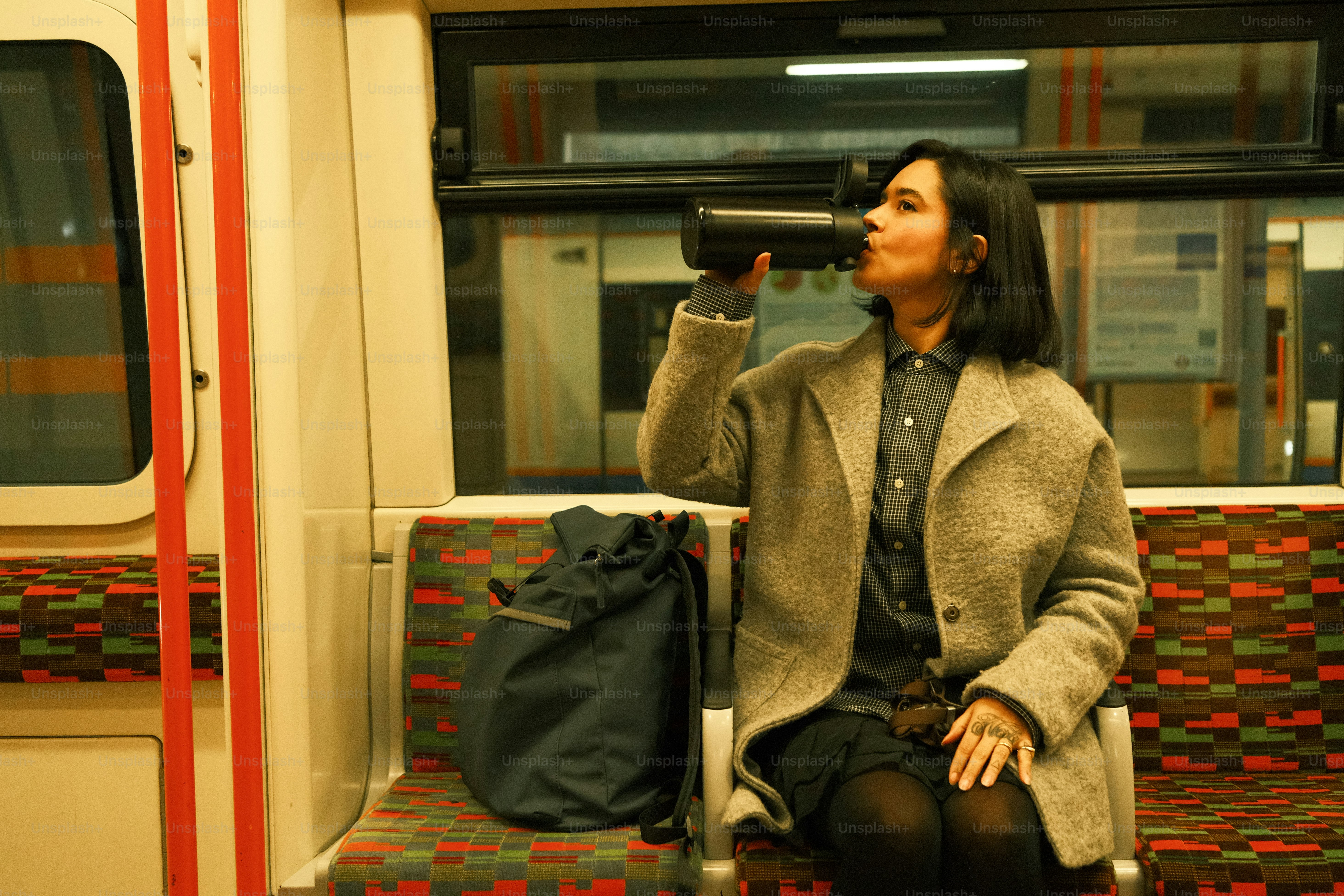 A woman sitting on a train drinking from a cup