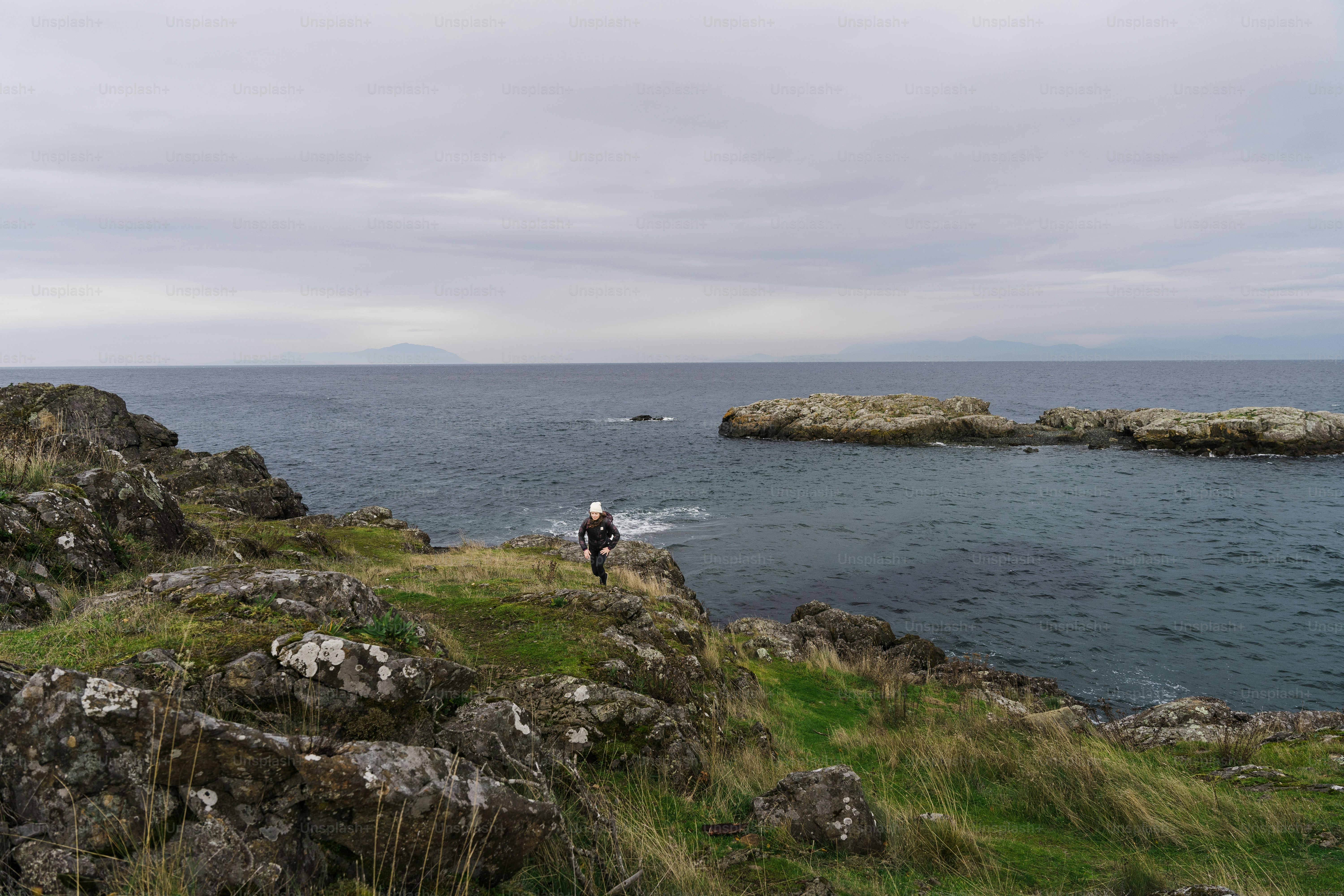 A man standing on top of a lush green hillside next to the ocean
