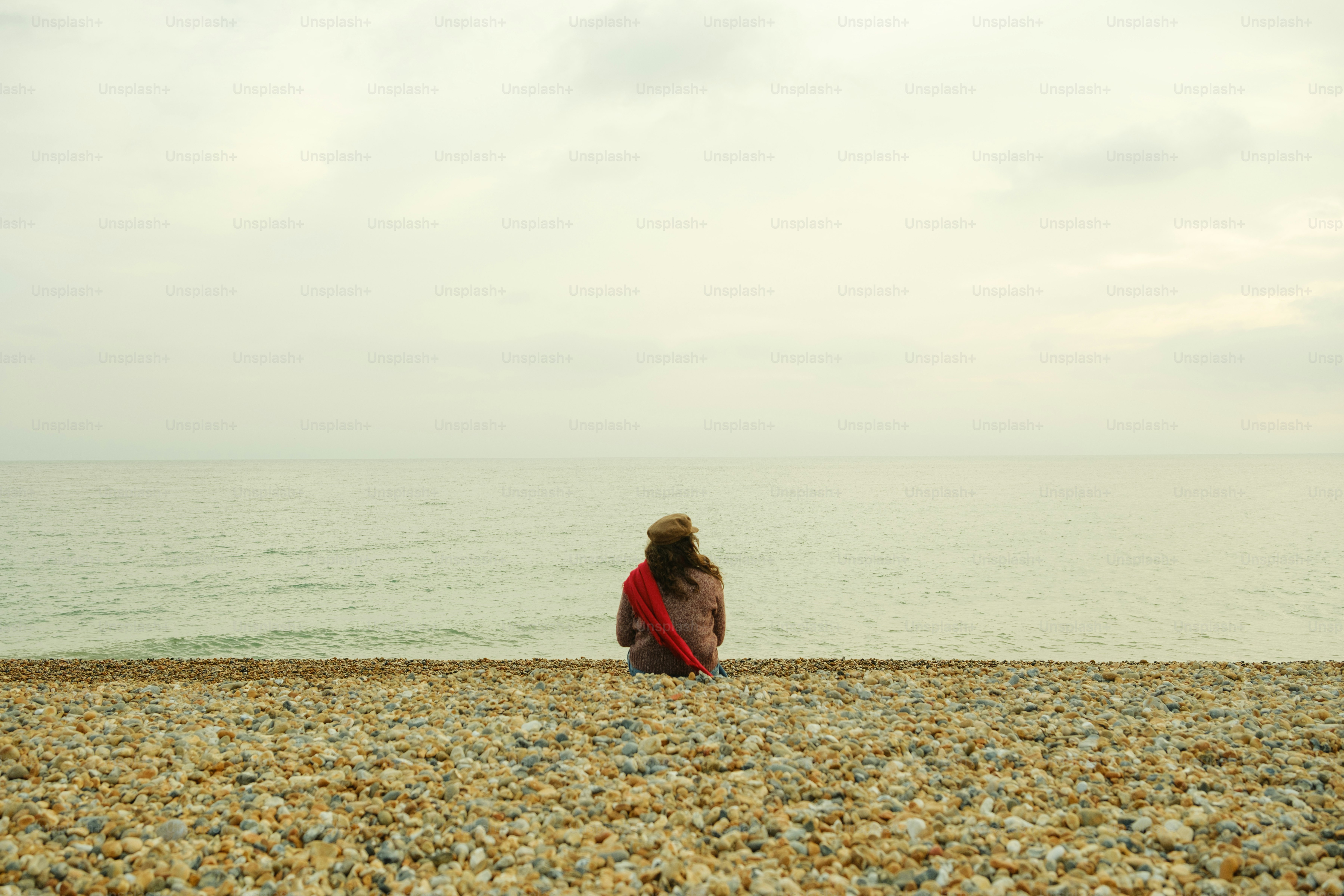 A woman sitting on a beach looking out at the ocean