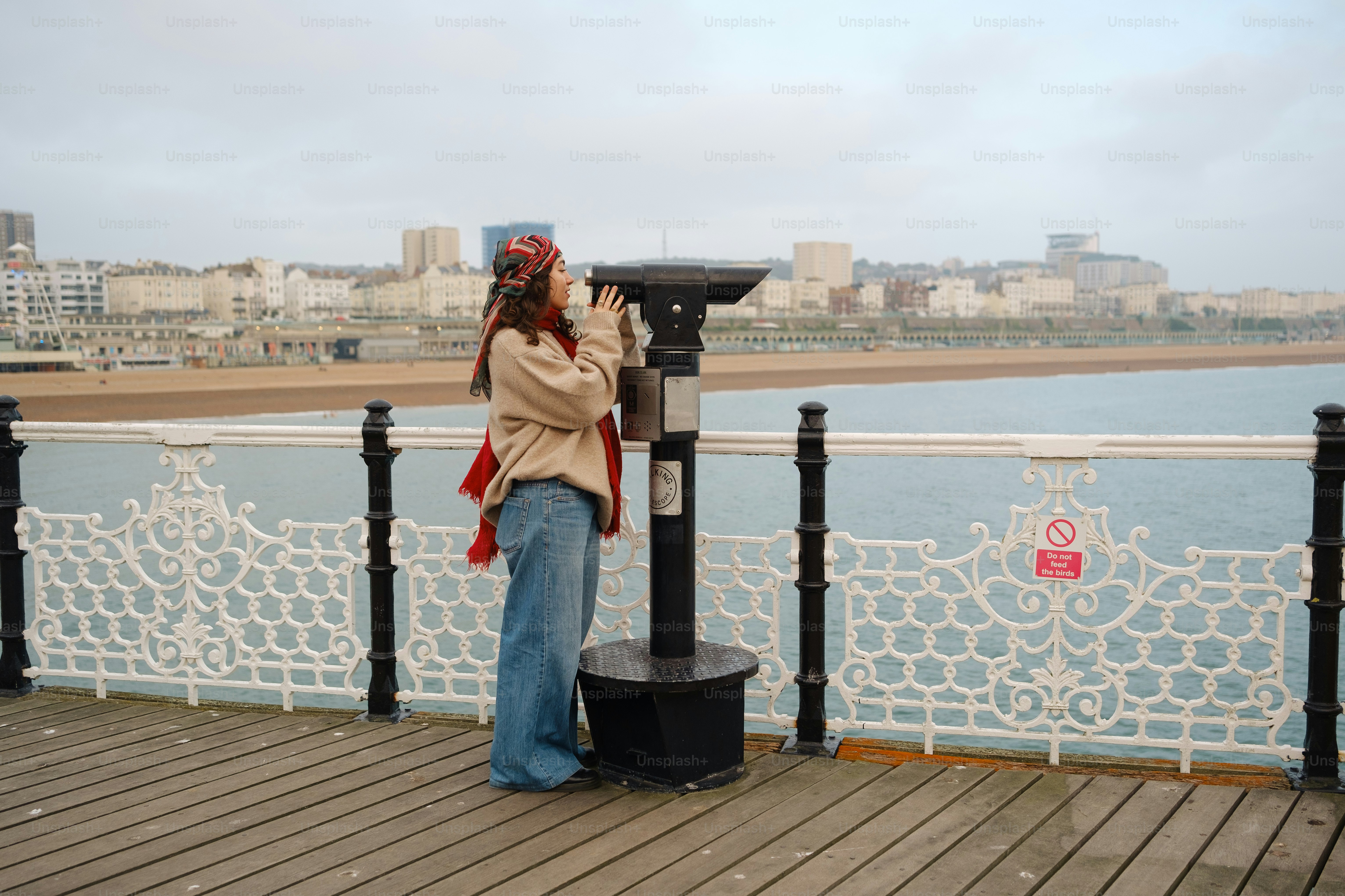 A woman standing on a pier next to a black trash can