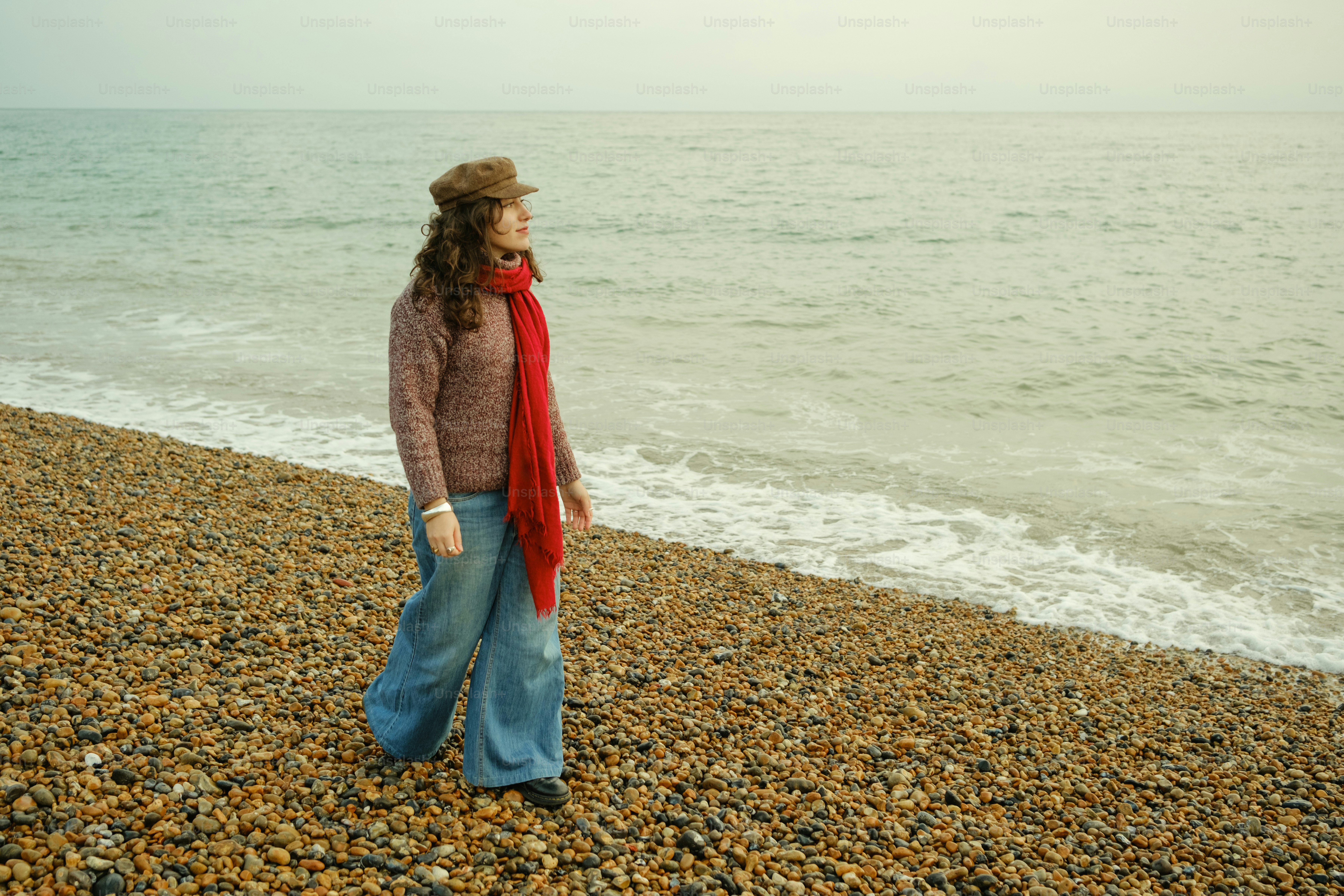 A woman standing on a rocky beach next to the ocean photo – Beach Image ...