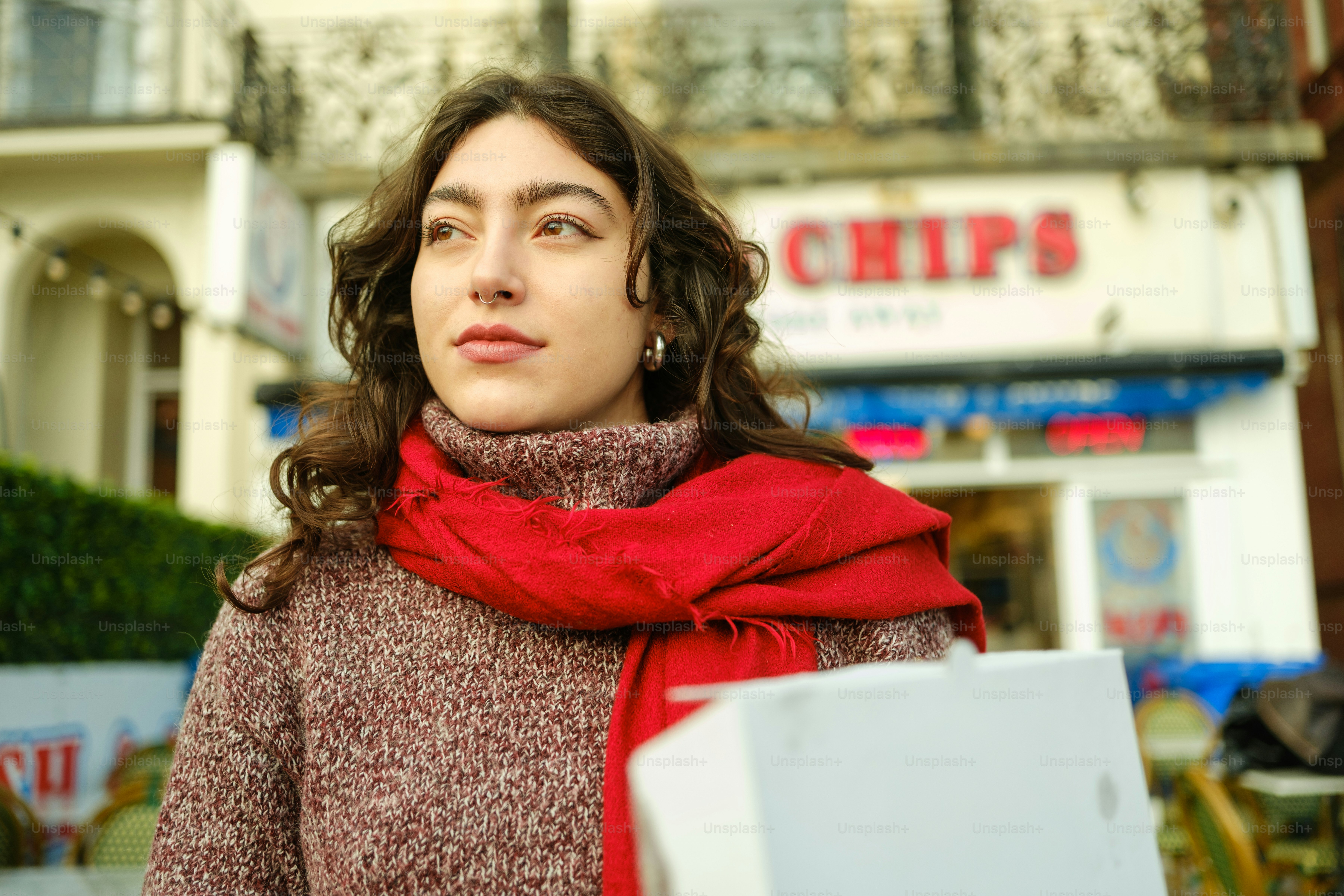 A woman standing in front of a building with a red scarf around her neck
