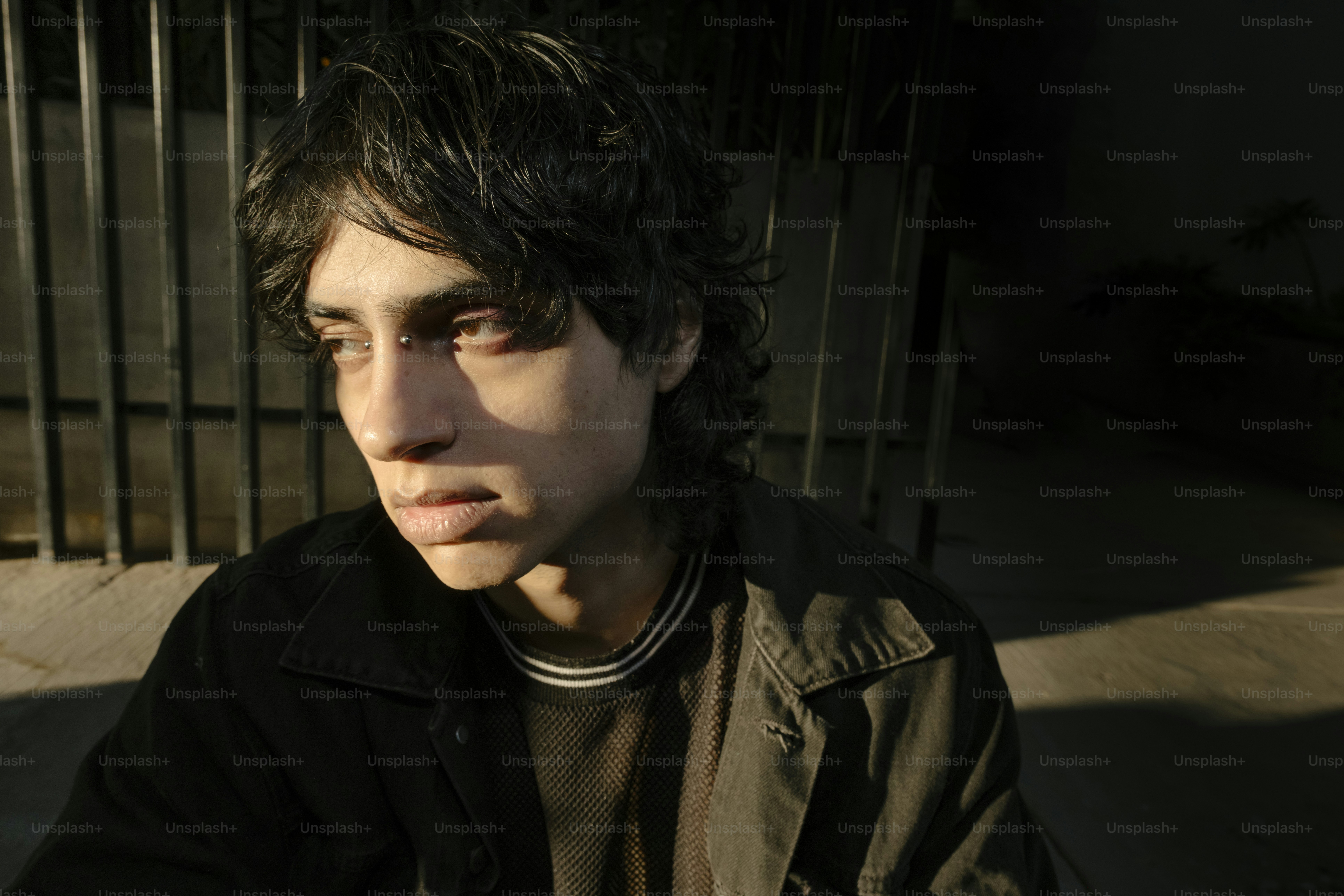 A young man sitting on the ground next to a fence