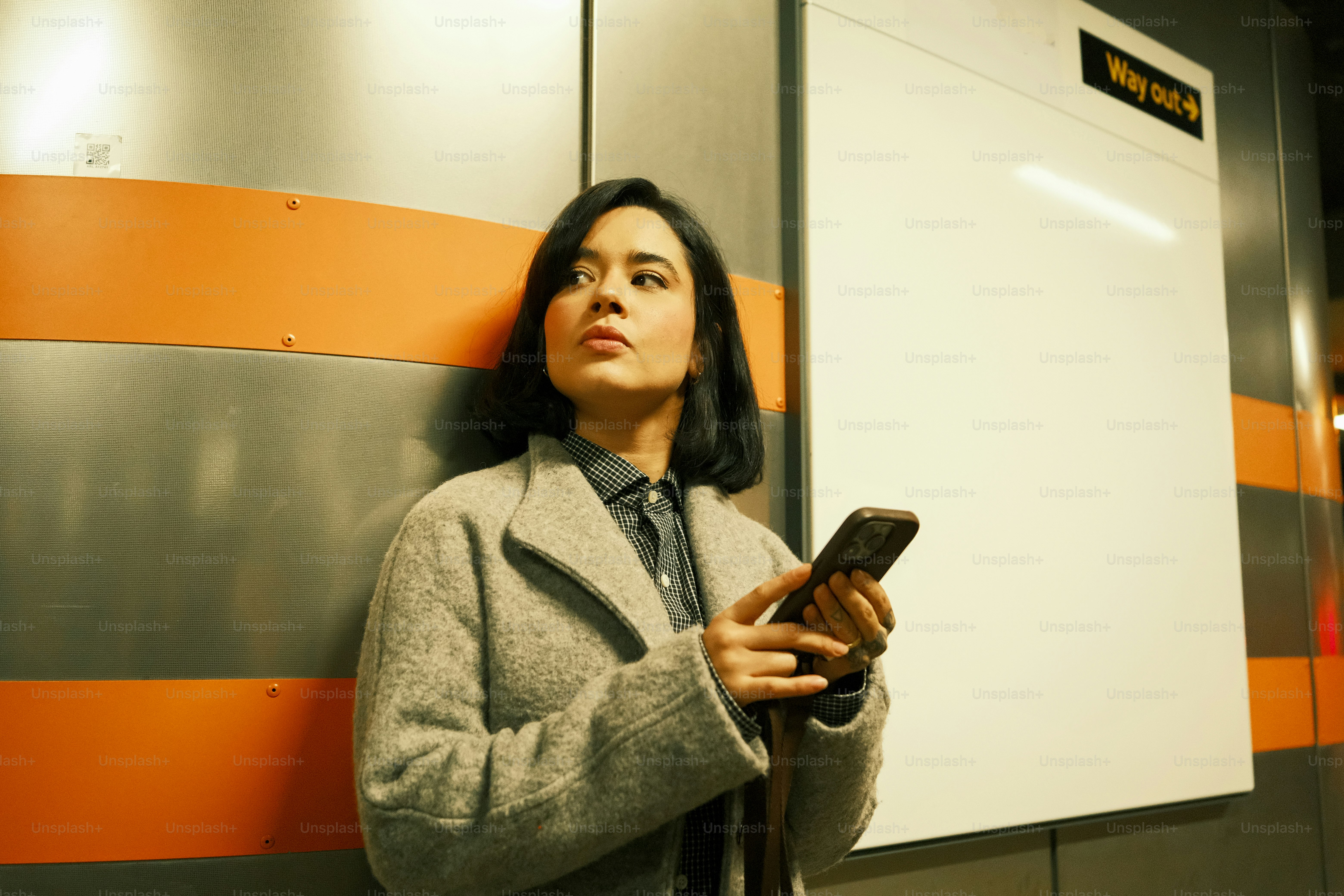 A woman leaning against a wall holding a cell phone