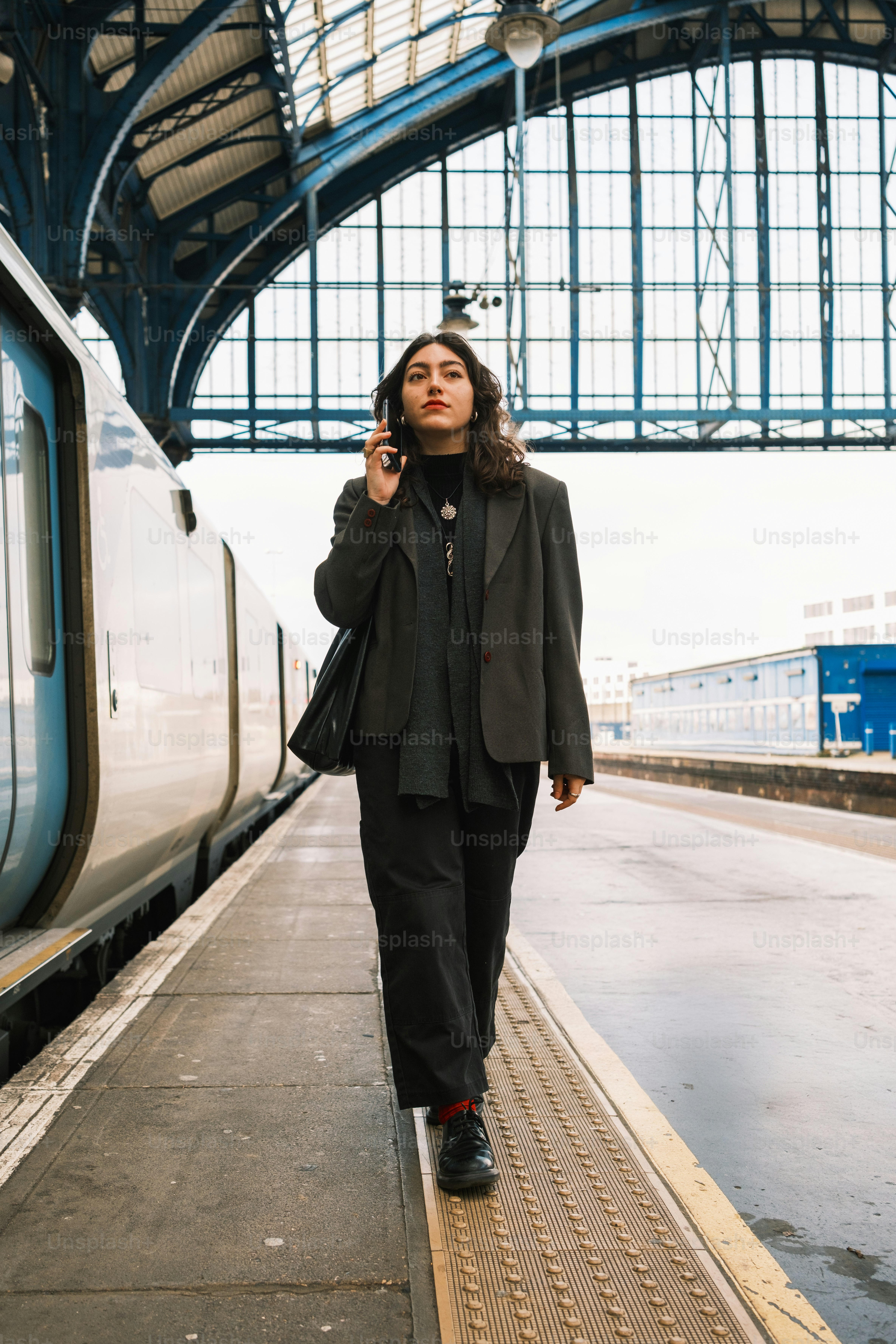 A woman walking on a train platform while talking on a cell phone