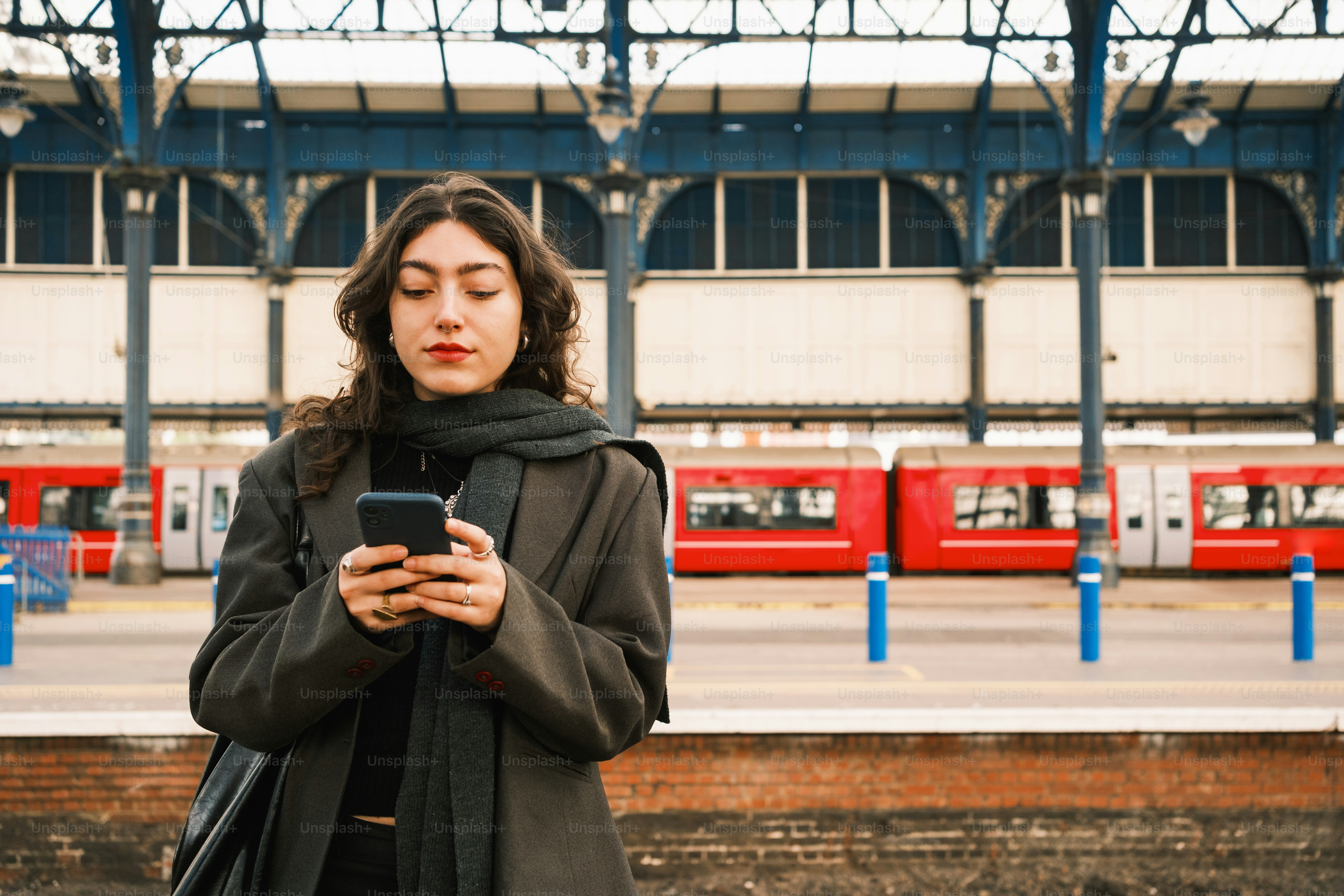A woman standing in front of a train station looking at her cell phone