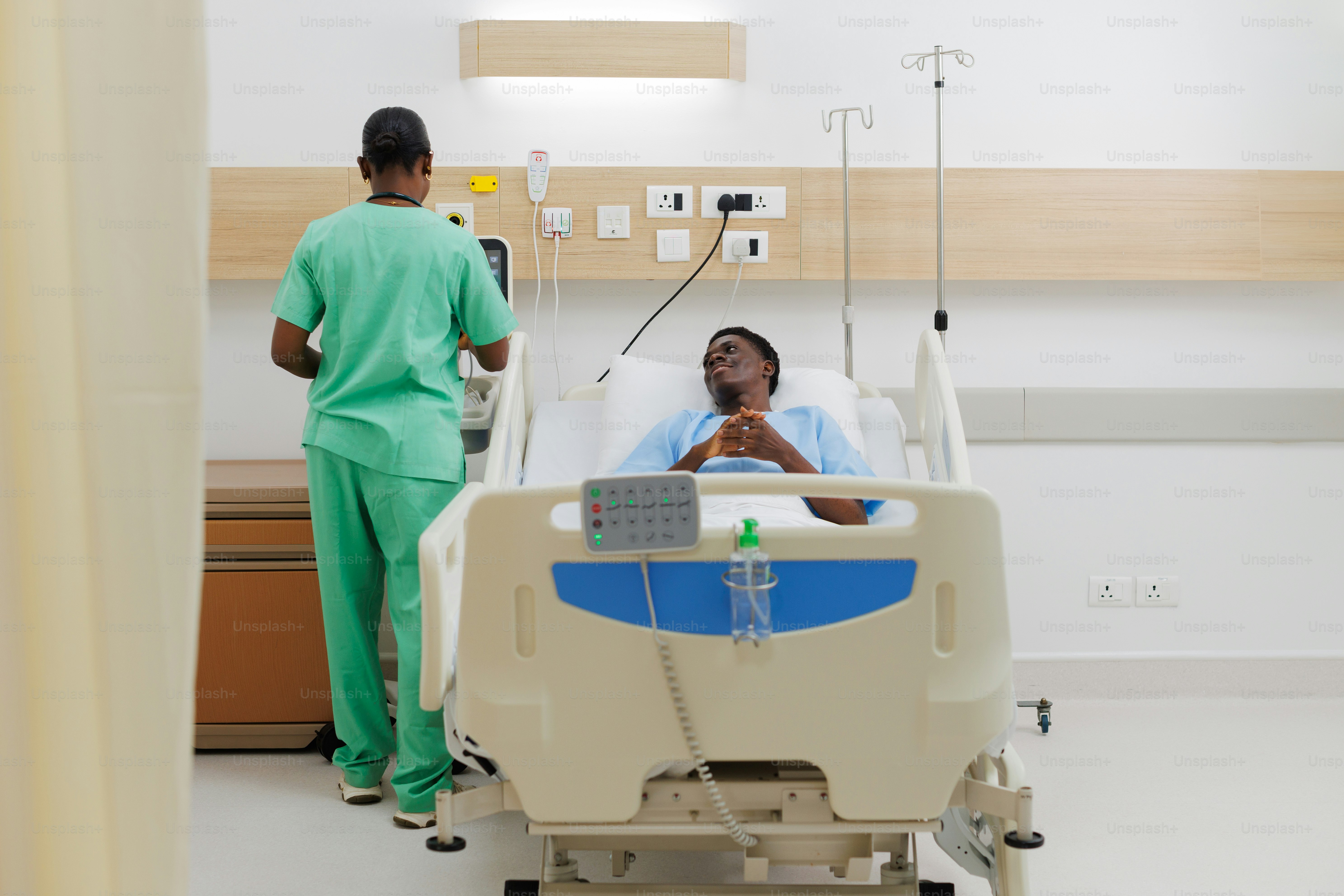 A woman in a hospital bed talking to a man in a green scrub suit