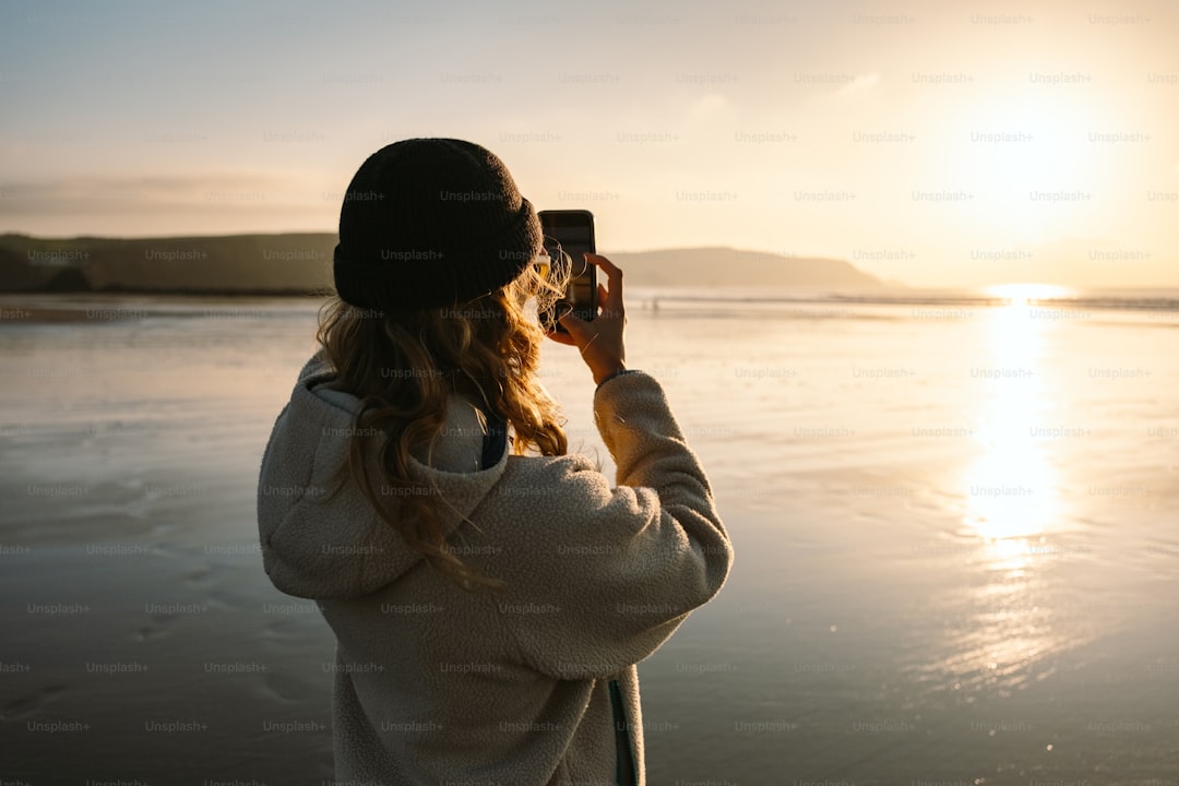 A woman taking a picture of the sun setting over a body of water