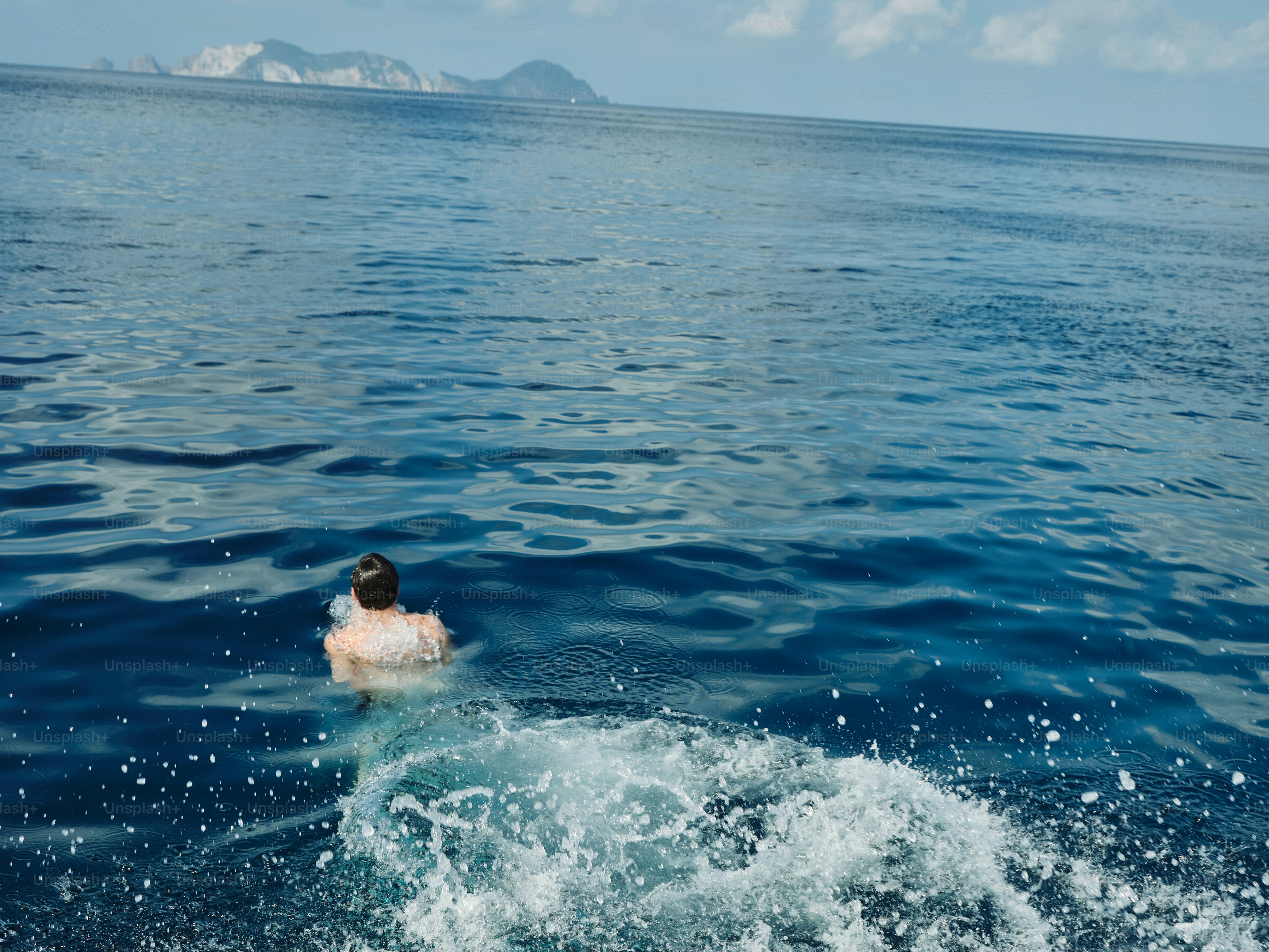 Un homme nageant dans l’océan avec un bateau en arrière-plan