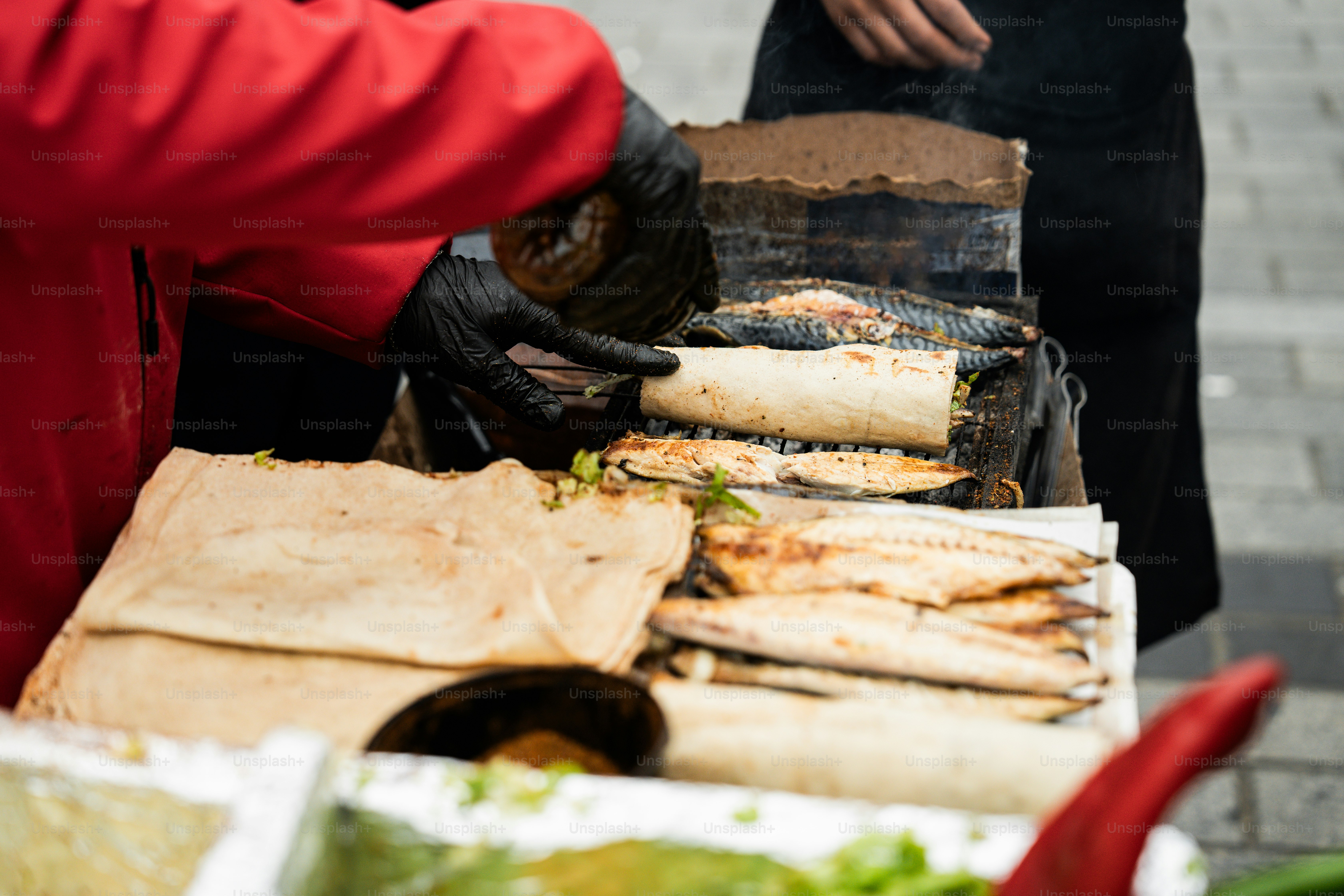 A person in a red jacket is cooking food on a grill