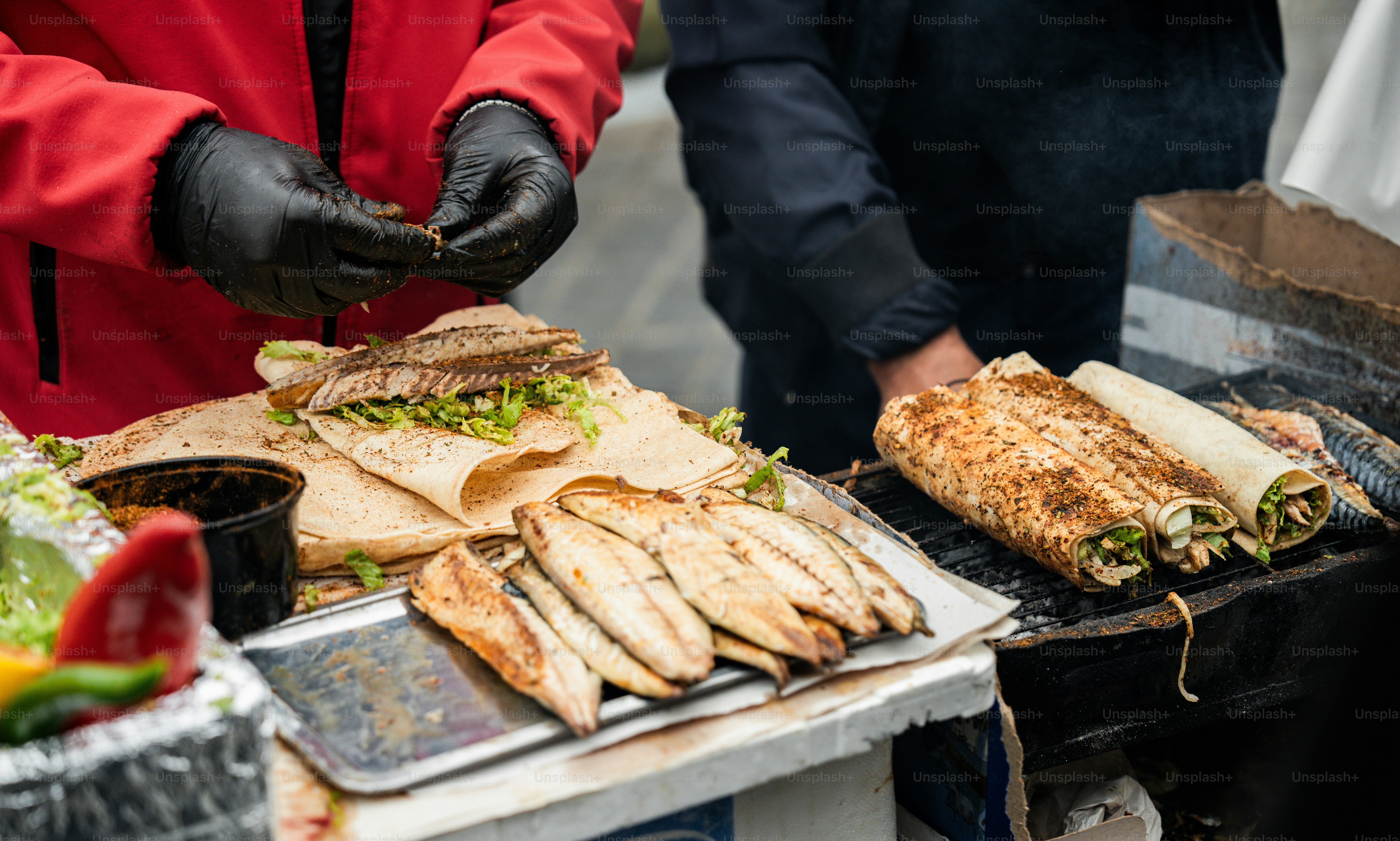 A person in a red jacket is cooking food on a grill