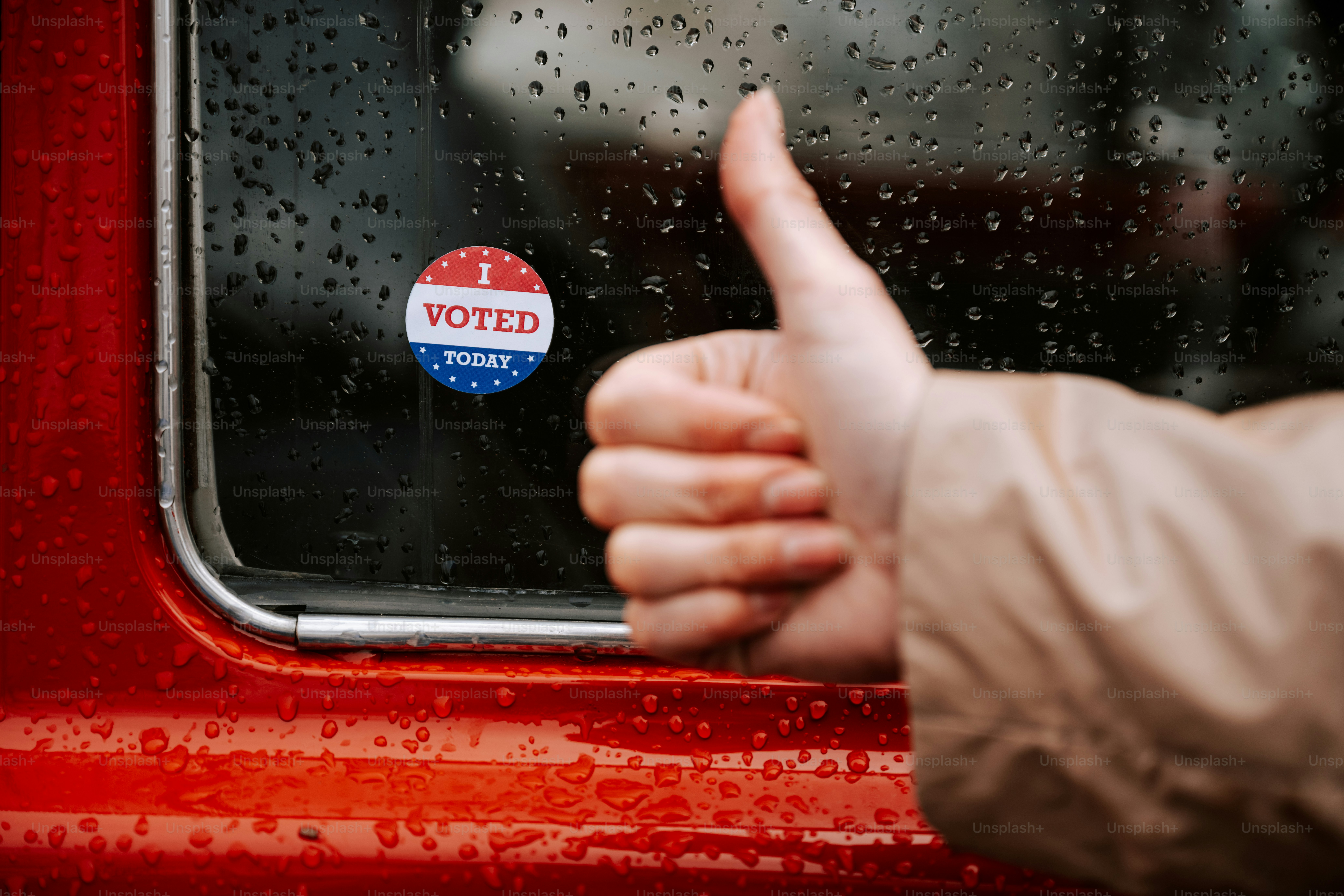 A person giving a thumbs up in front of a red car
