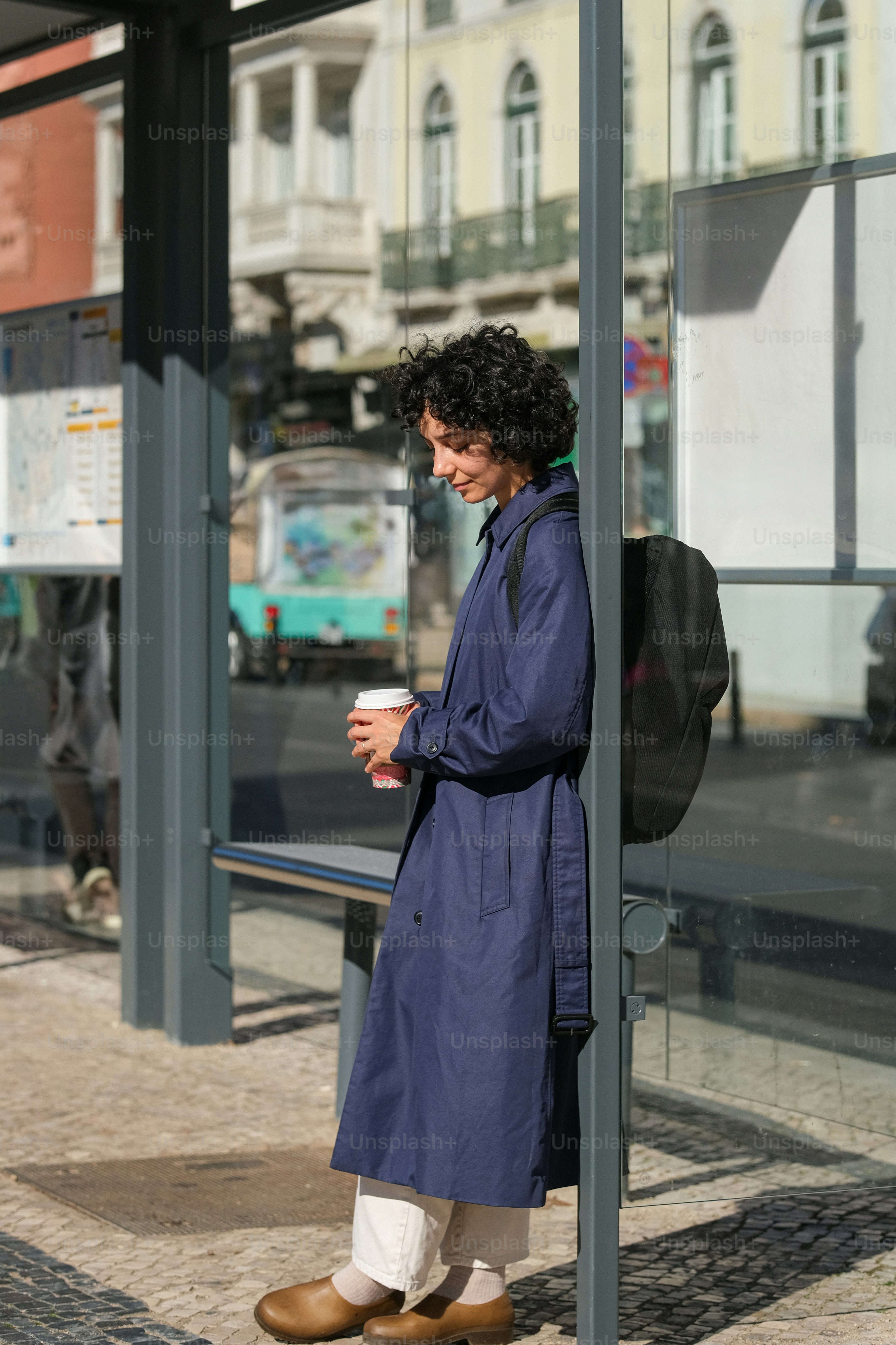 A woman standing in front of a bus stop holding a cup of coffee