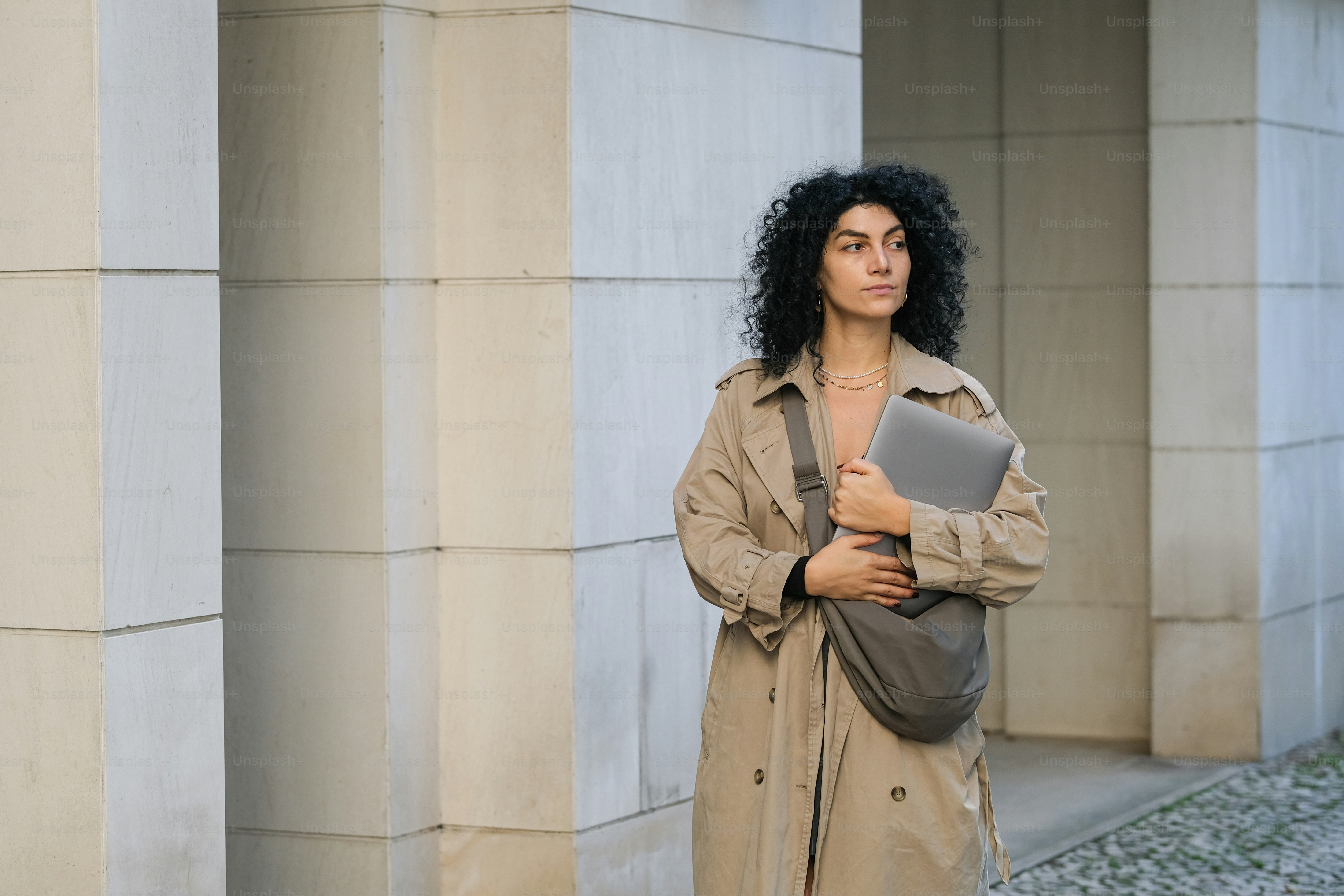 A woman in a trench coat is holding a laptop