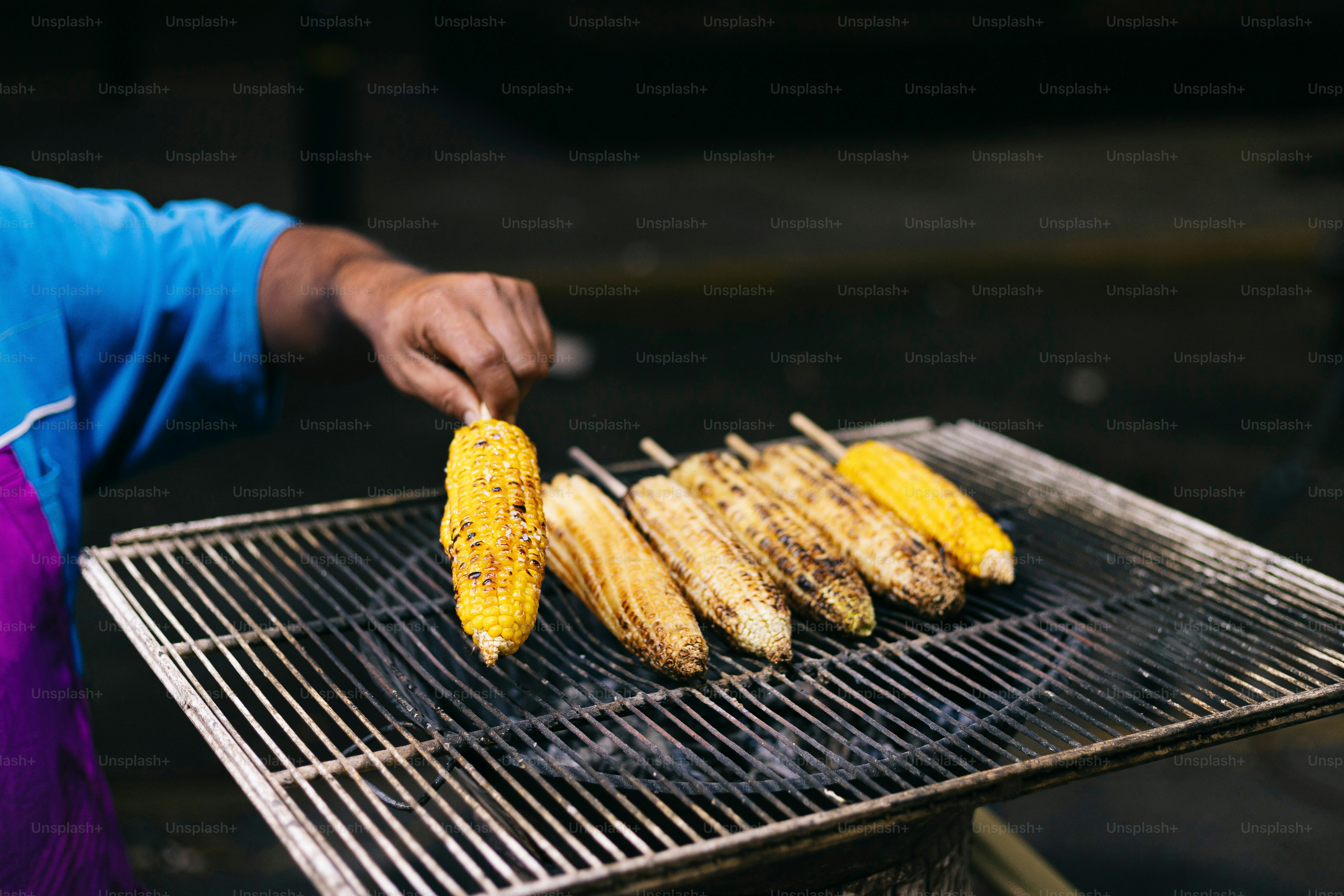 Una persona asando mazorcas de maíz en una parrilla