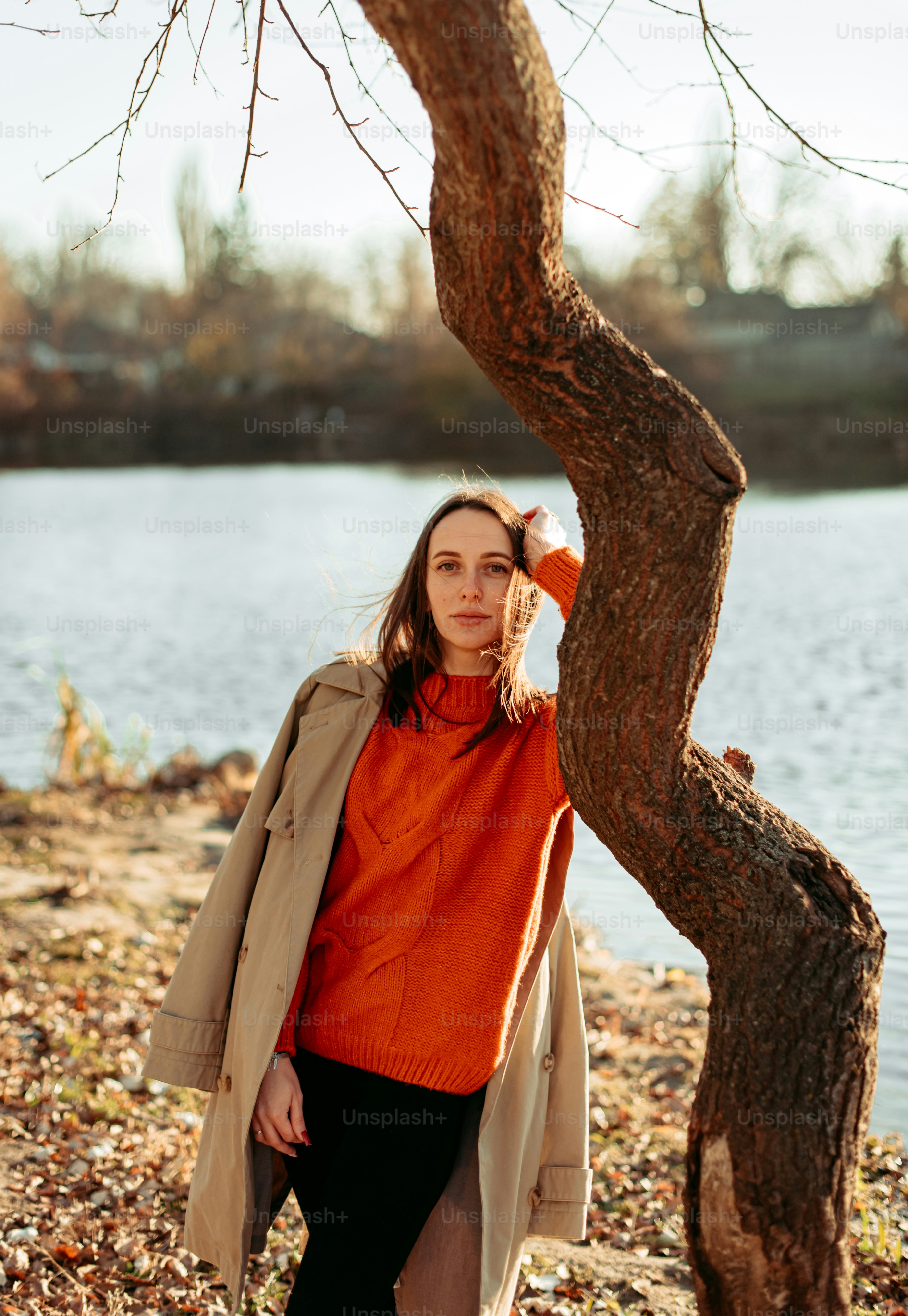 A woman standing next to a tree near a body of water