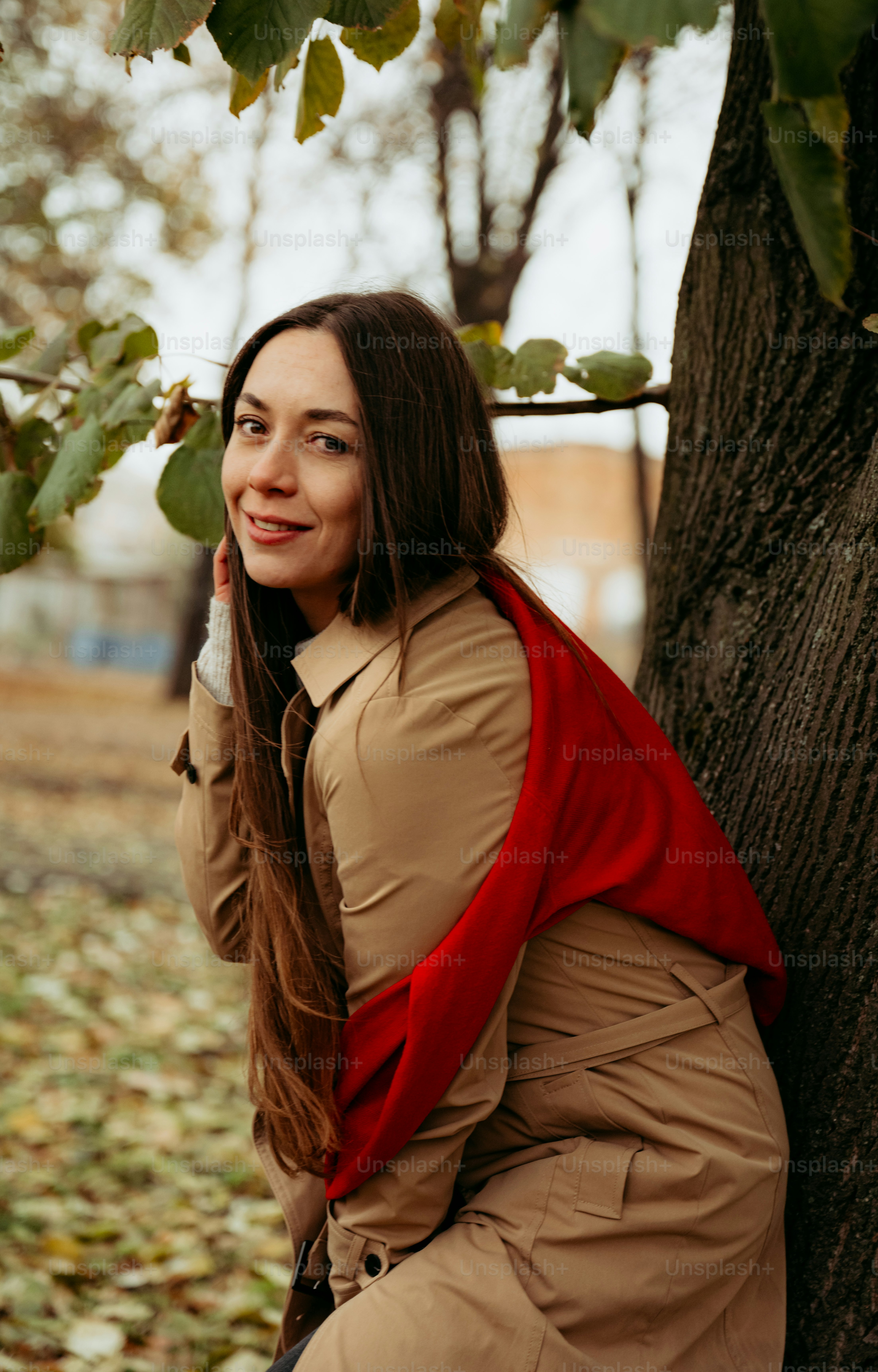 A woman leaning against a tree talking on a cell phone