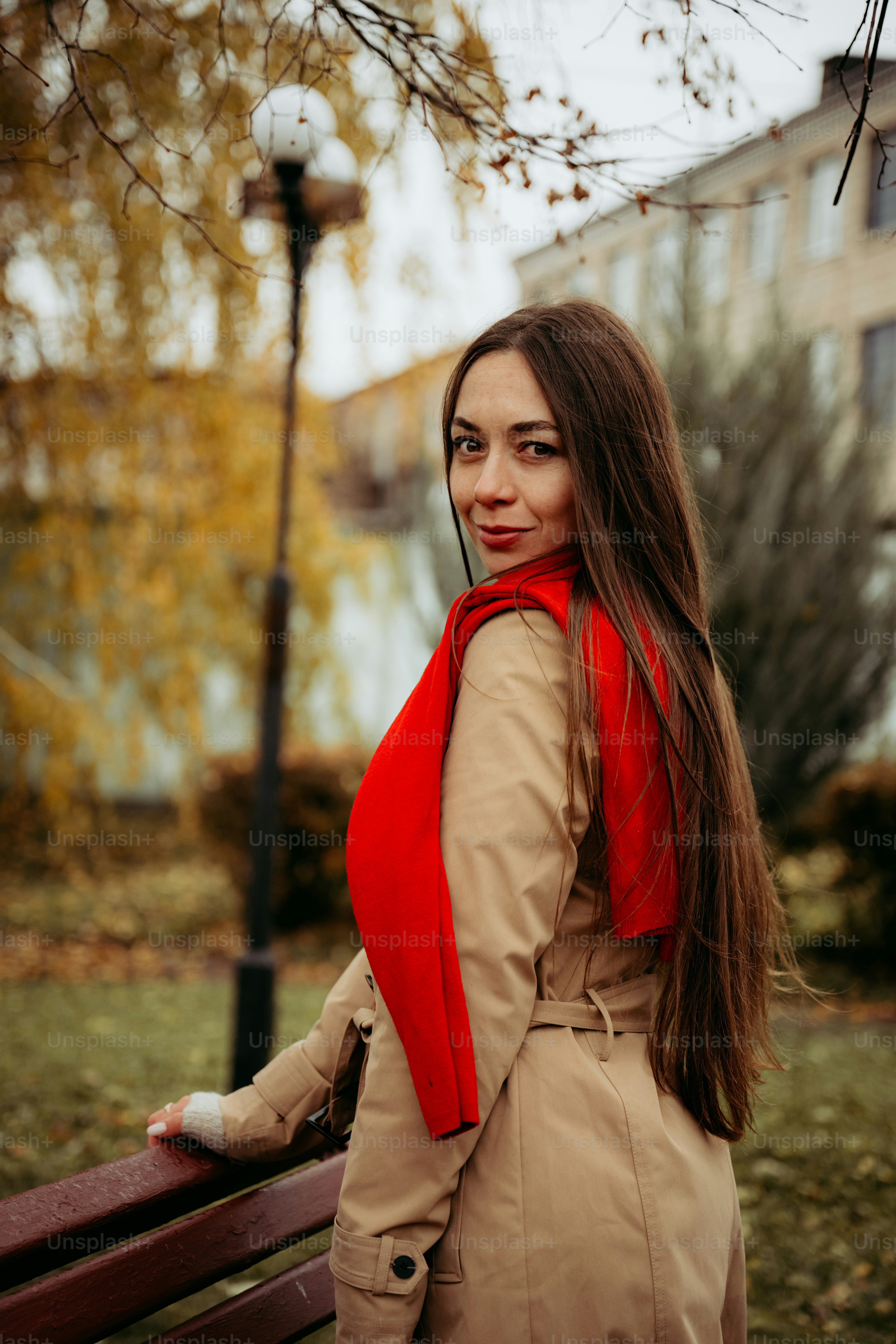 A woman in a trench coat is standing on a bench