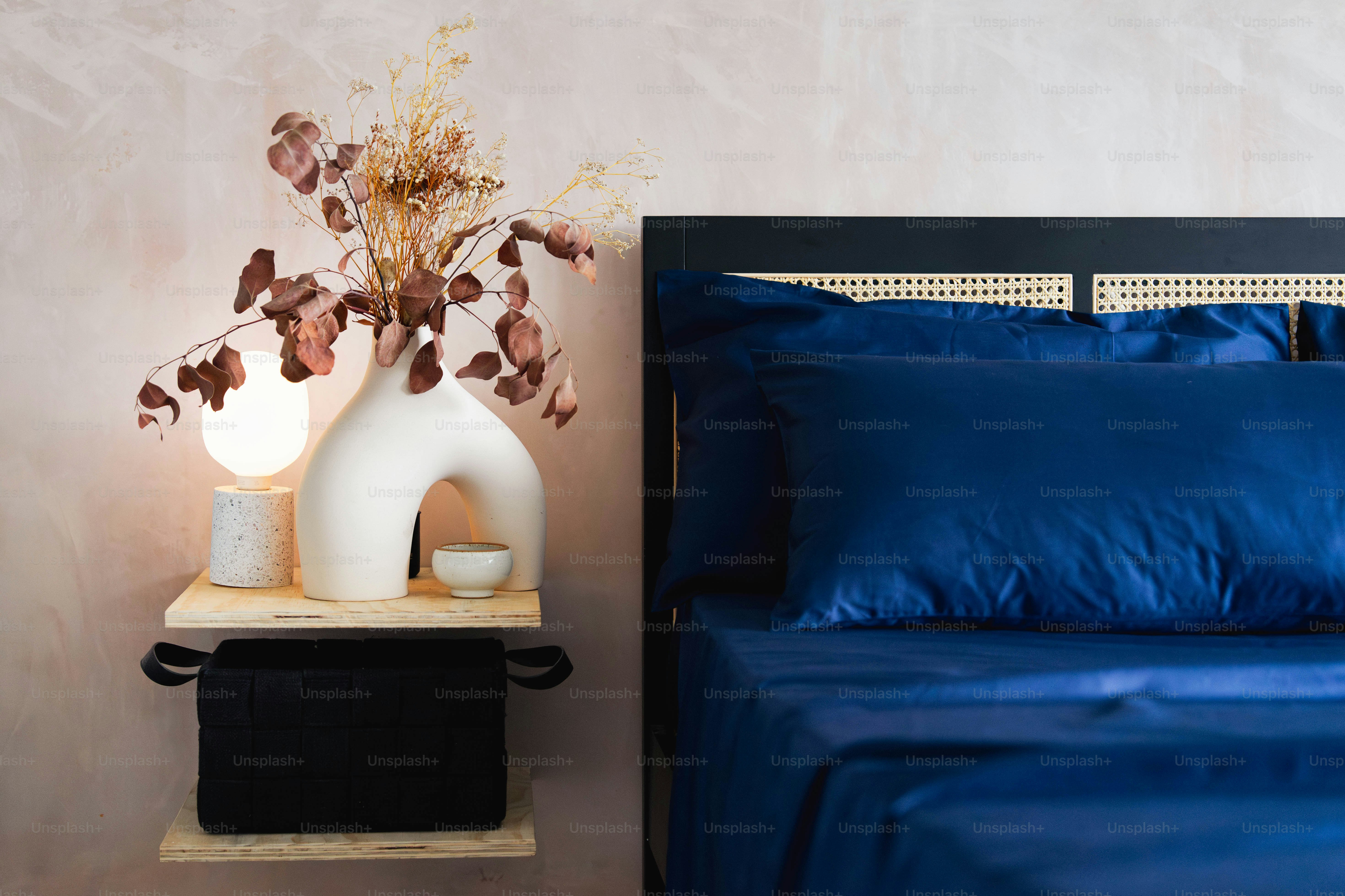 Una cama con sábanas azules y un jarrón blanco con flores