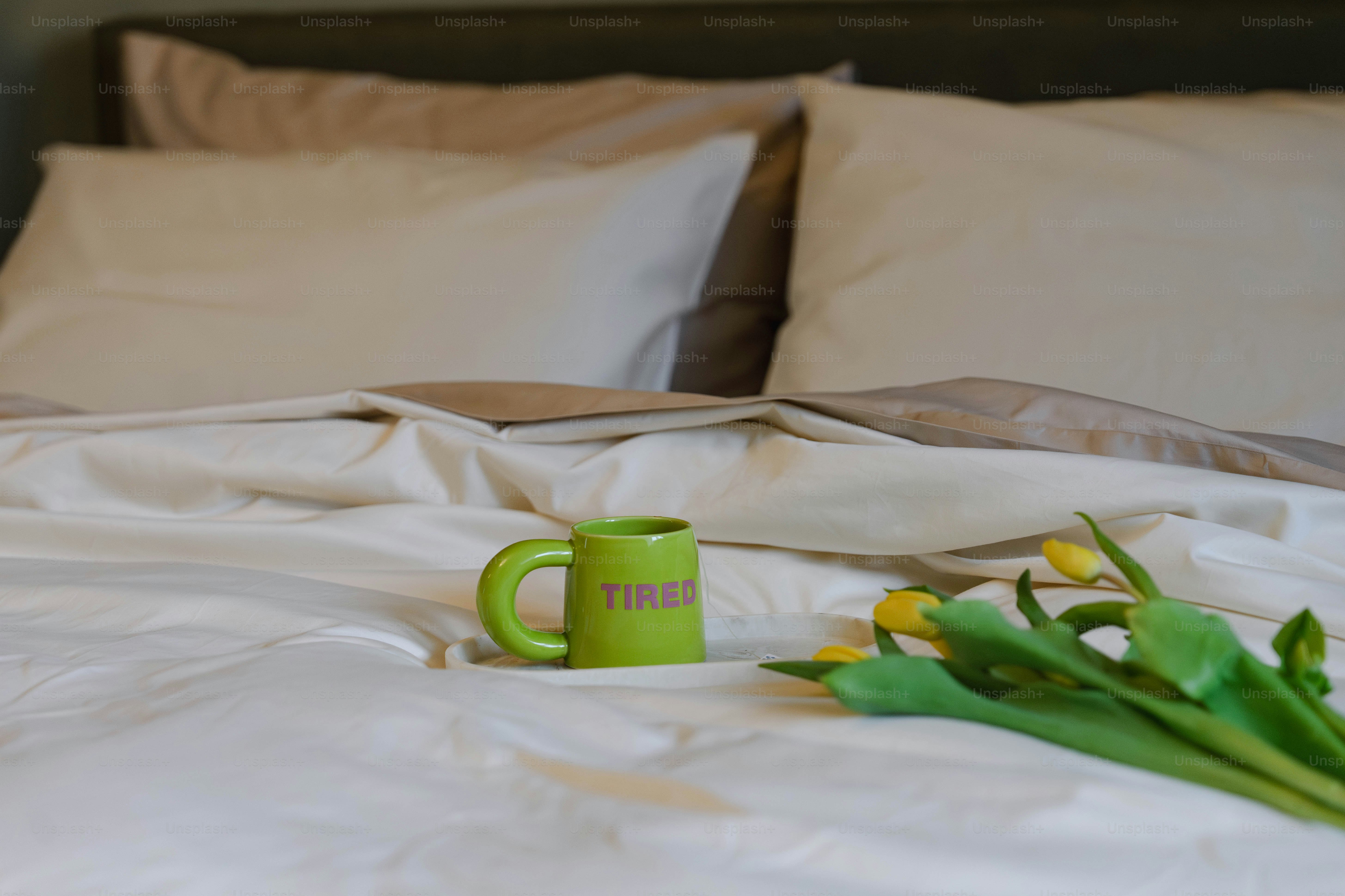A bed with a white comforter and a green coffee mug on it