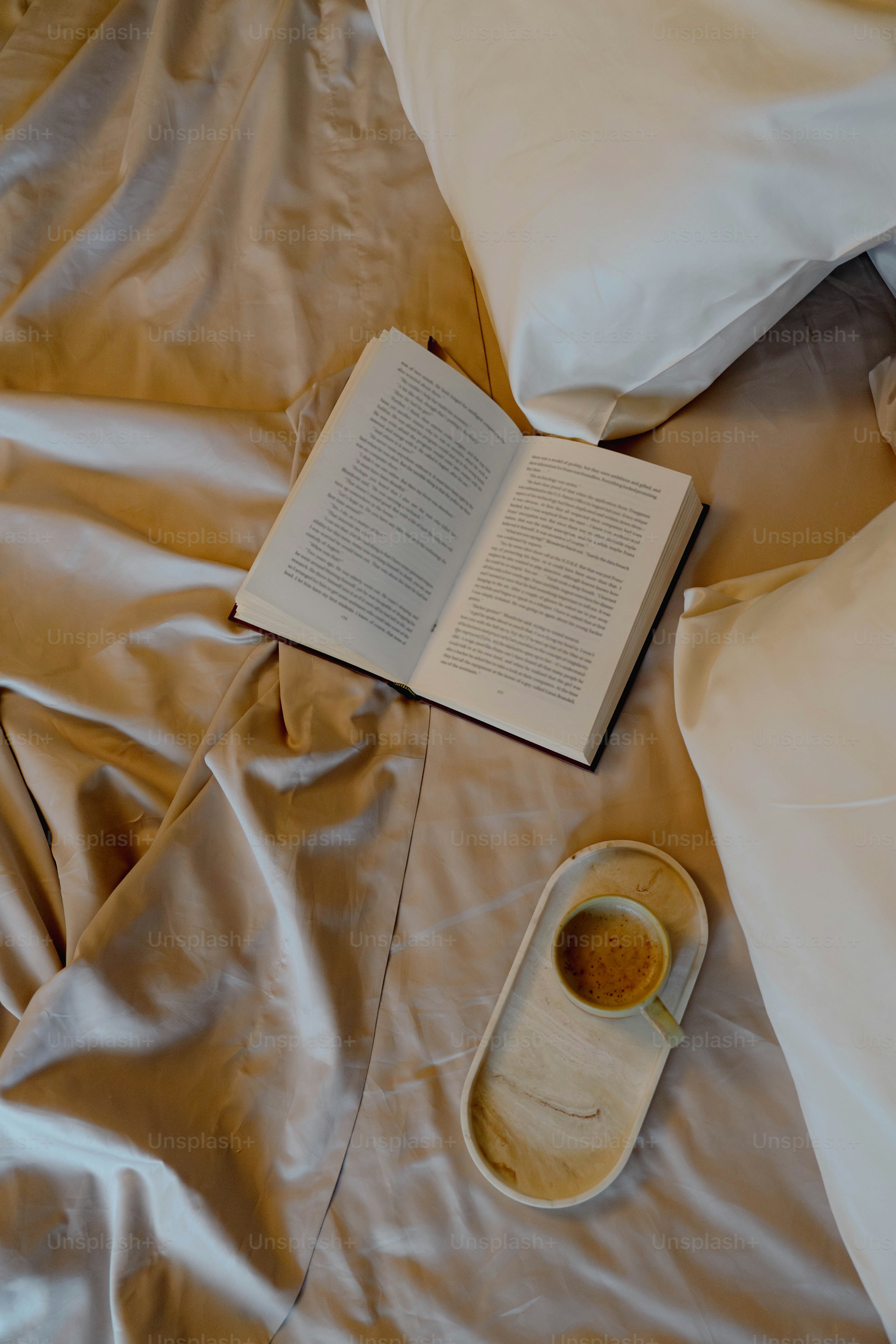 Un libro abierto y una taza de café en una cama