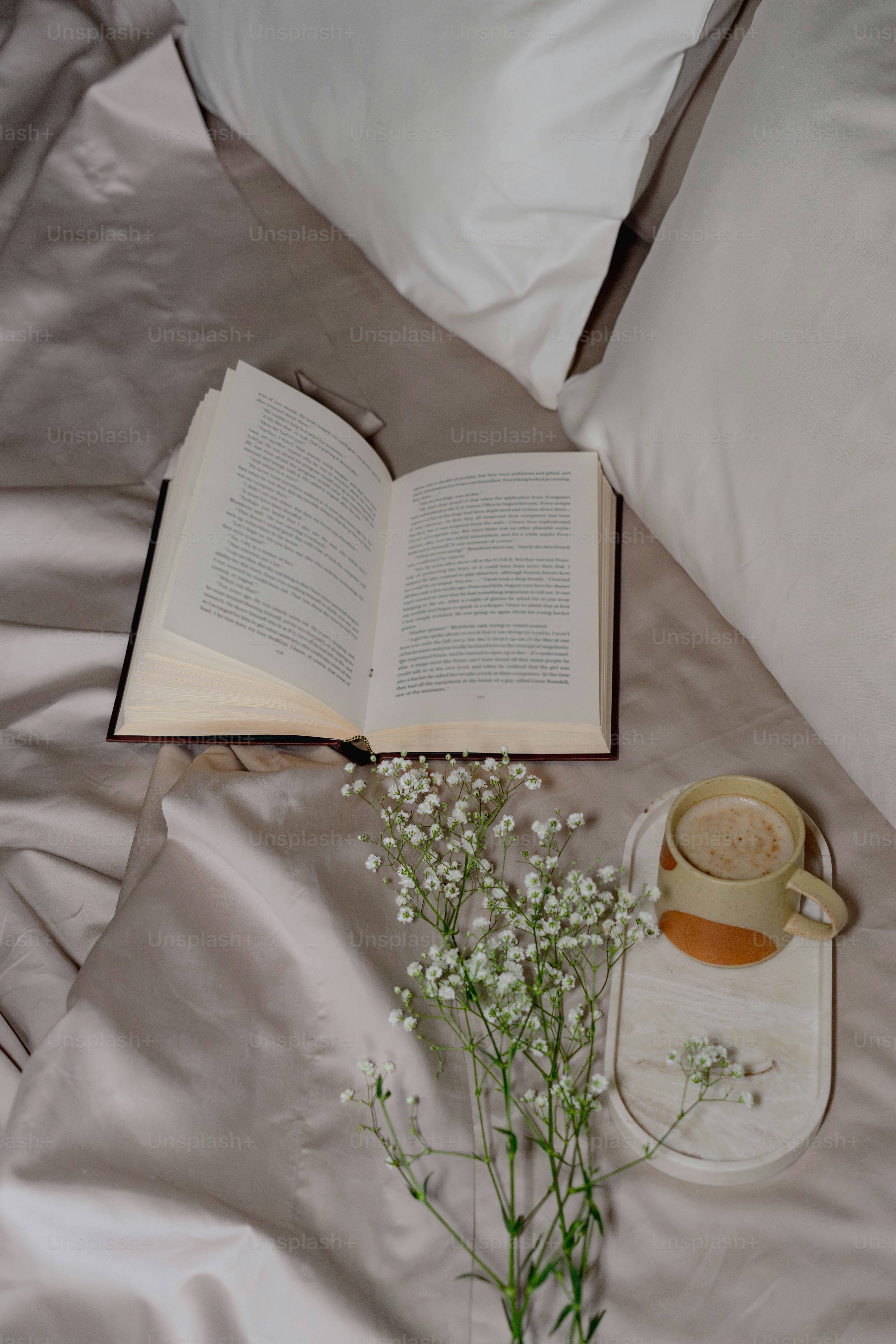 An open book on a bed next to a vase with flowers