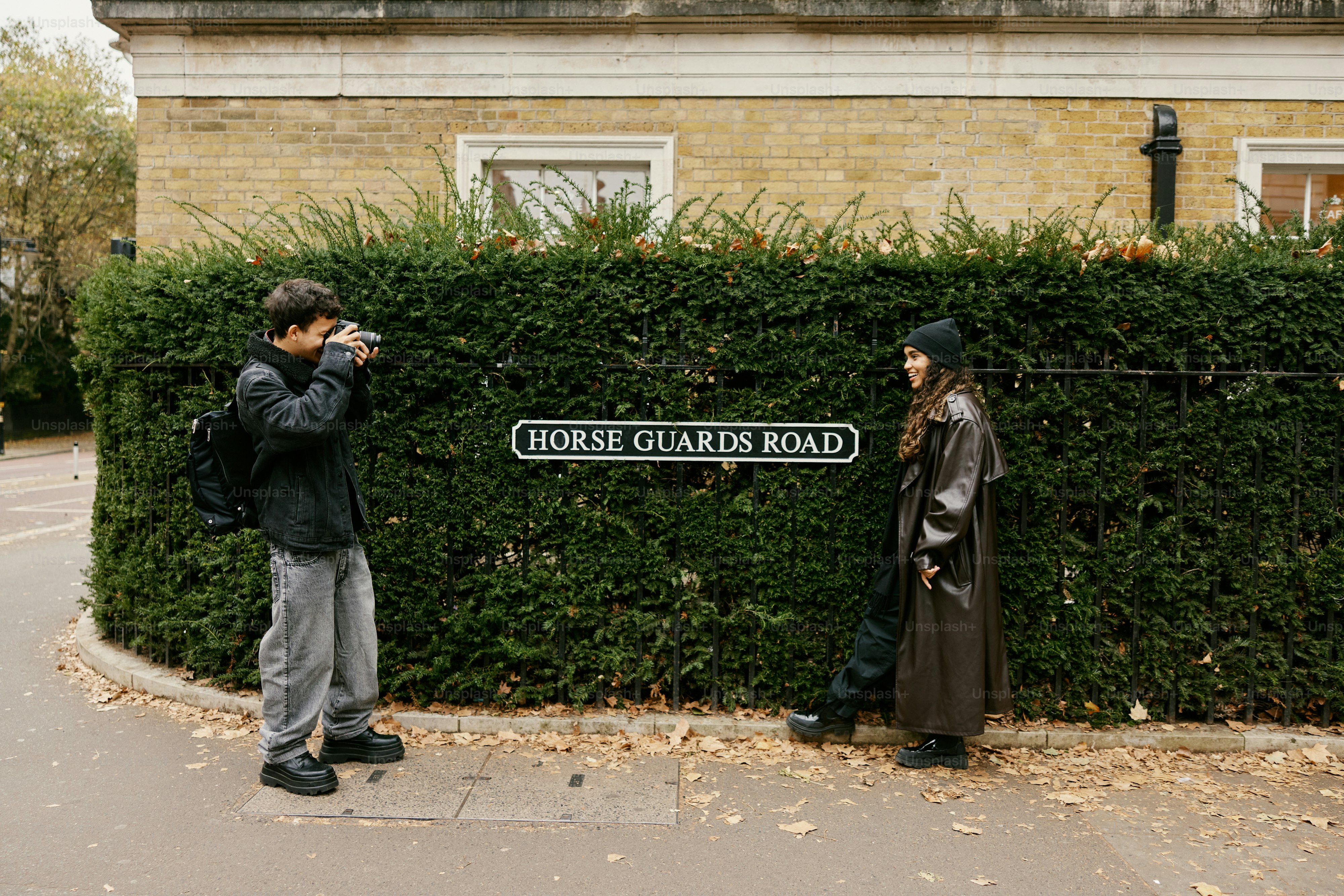 A man taking a picture of a woman standing in front of a hedge