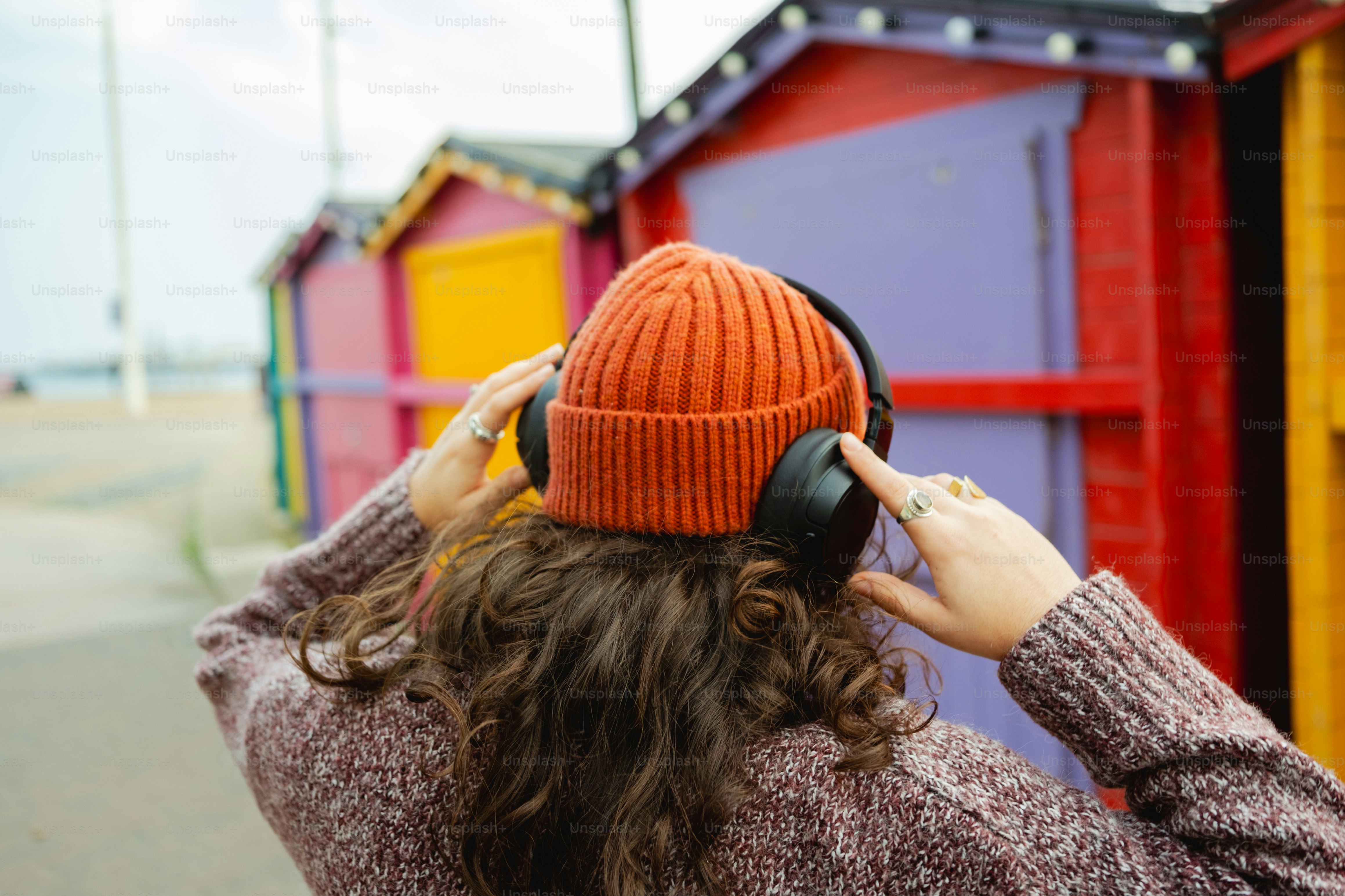 A woman listening to headphones in front of a row of beach huts
