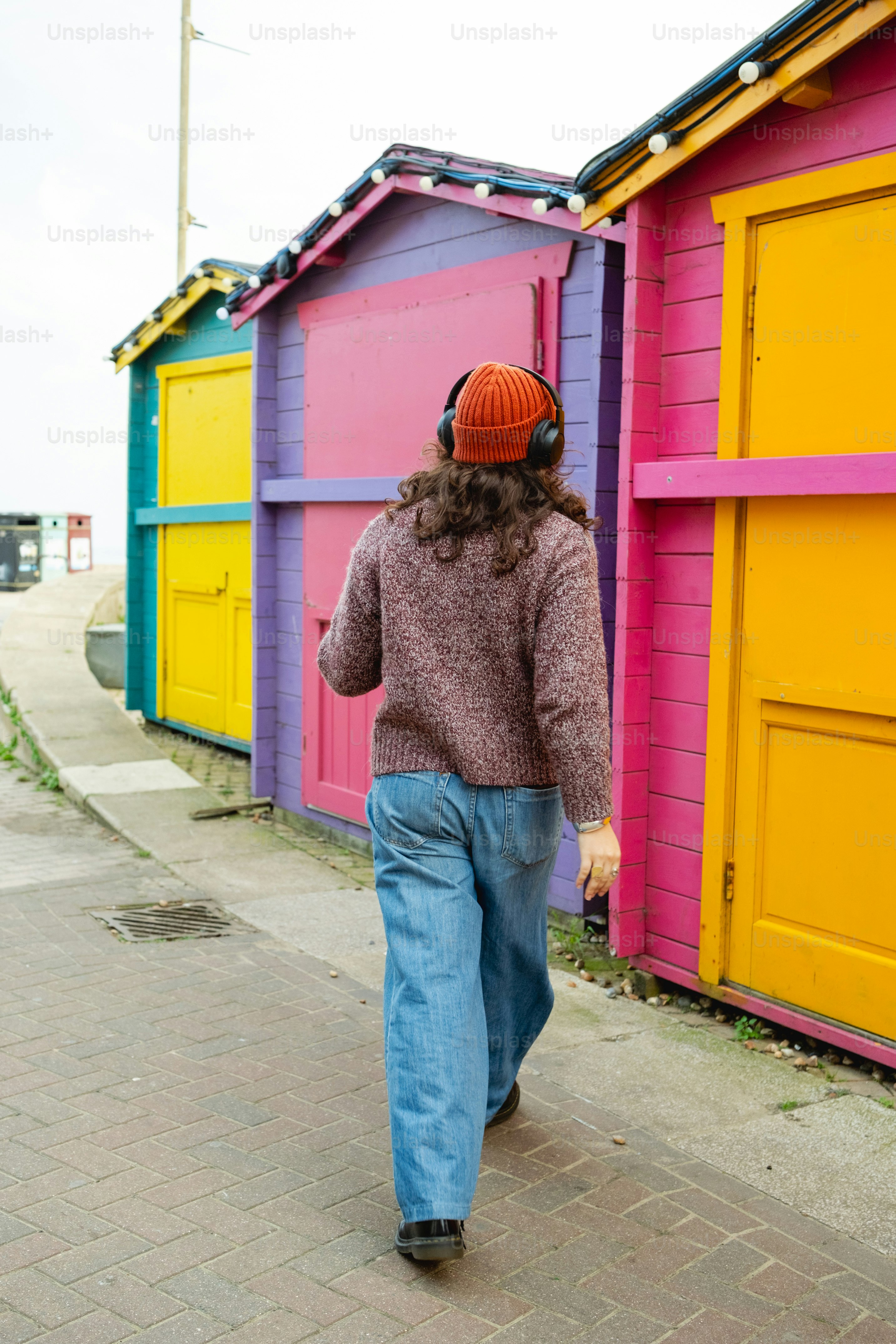 A woman walking down a sidewalk past colorful beach huts