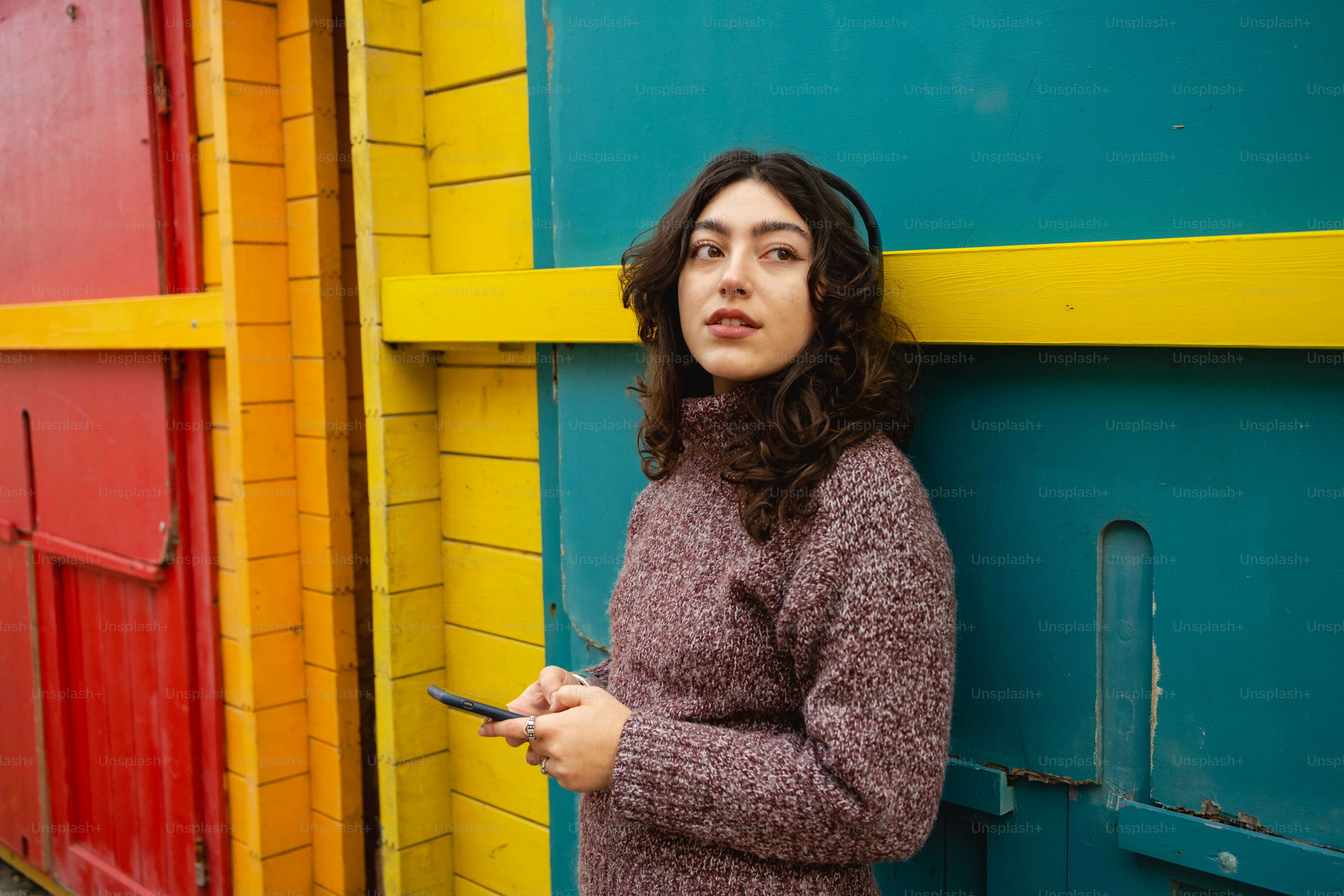 A woman leaning against a colorful wall holding a cell phone