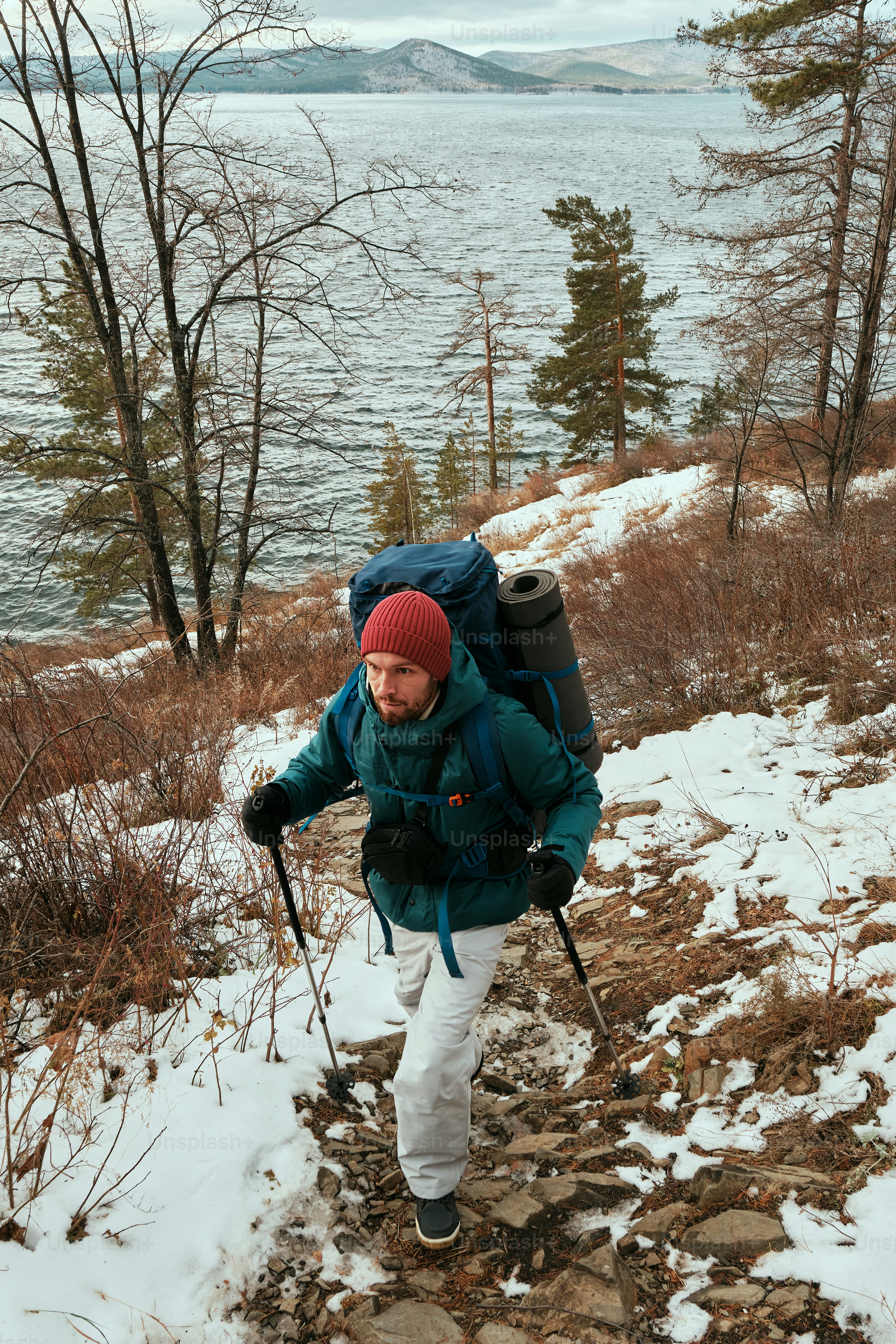 A man with a backpack is hiking up a snowy hill