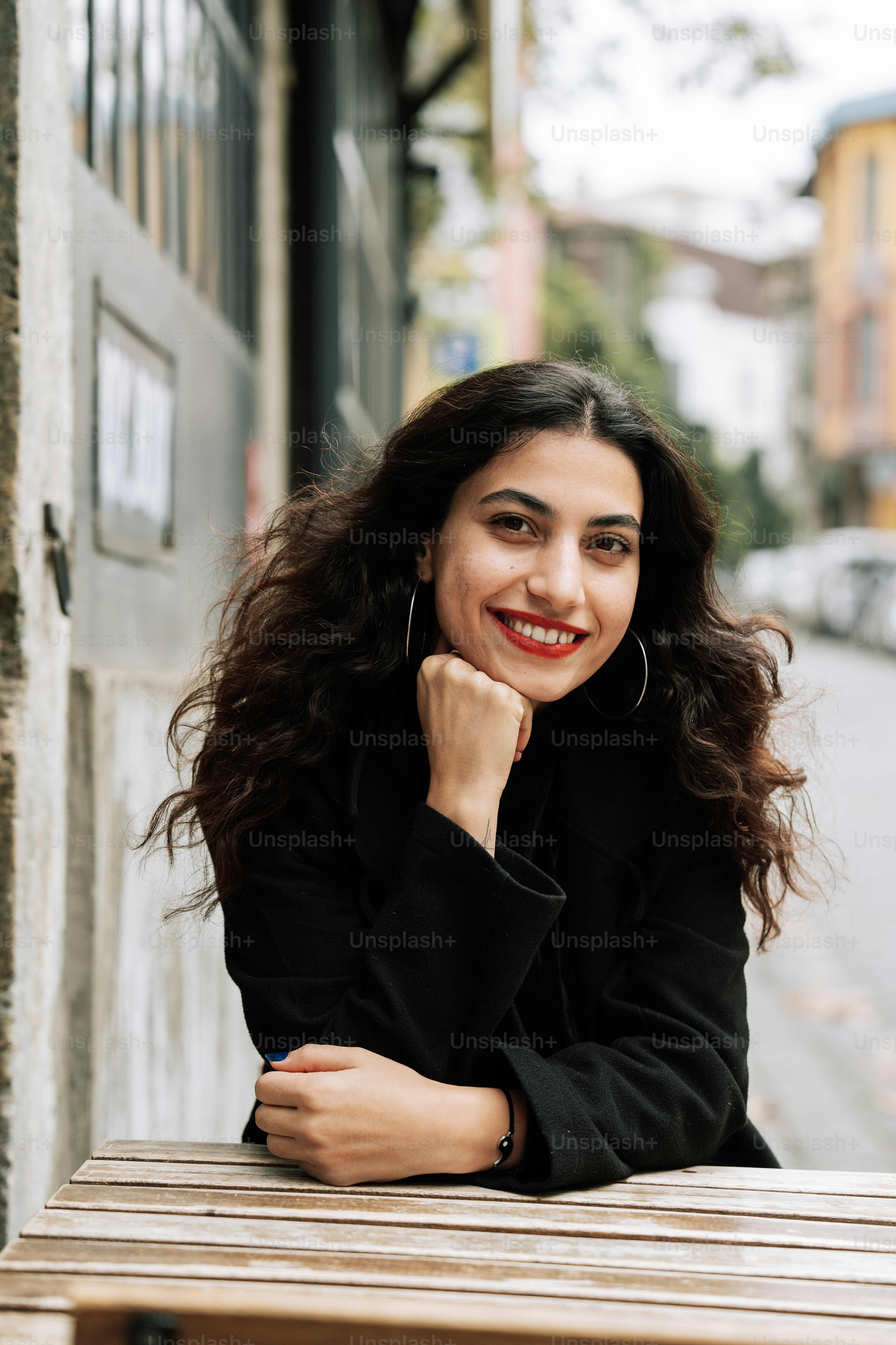 A woman sitting on a bench in front of a building photo – Profile Image ...