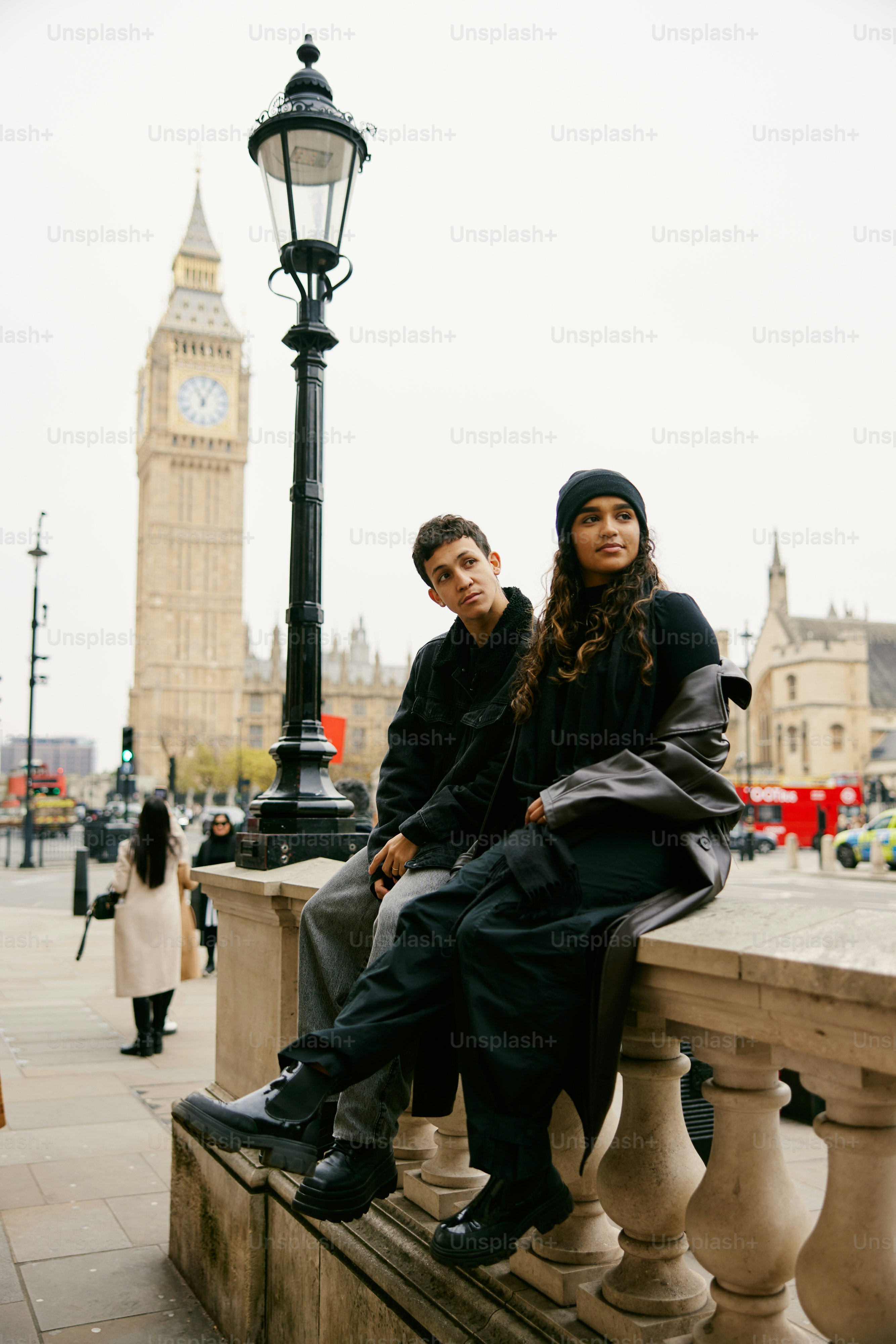 A man and a woman sitting on a bench in front of a clock tower