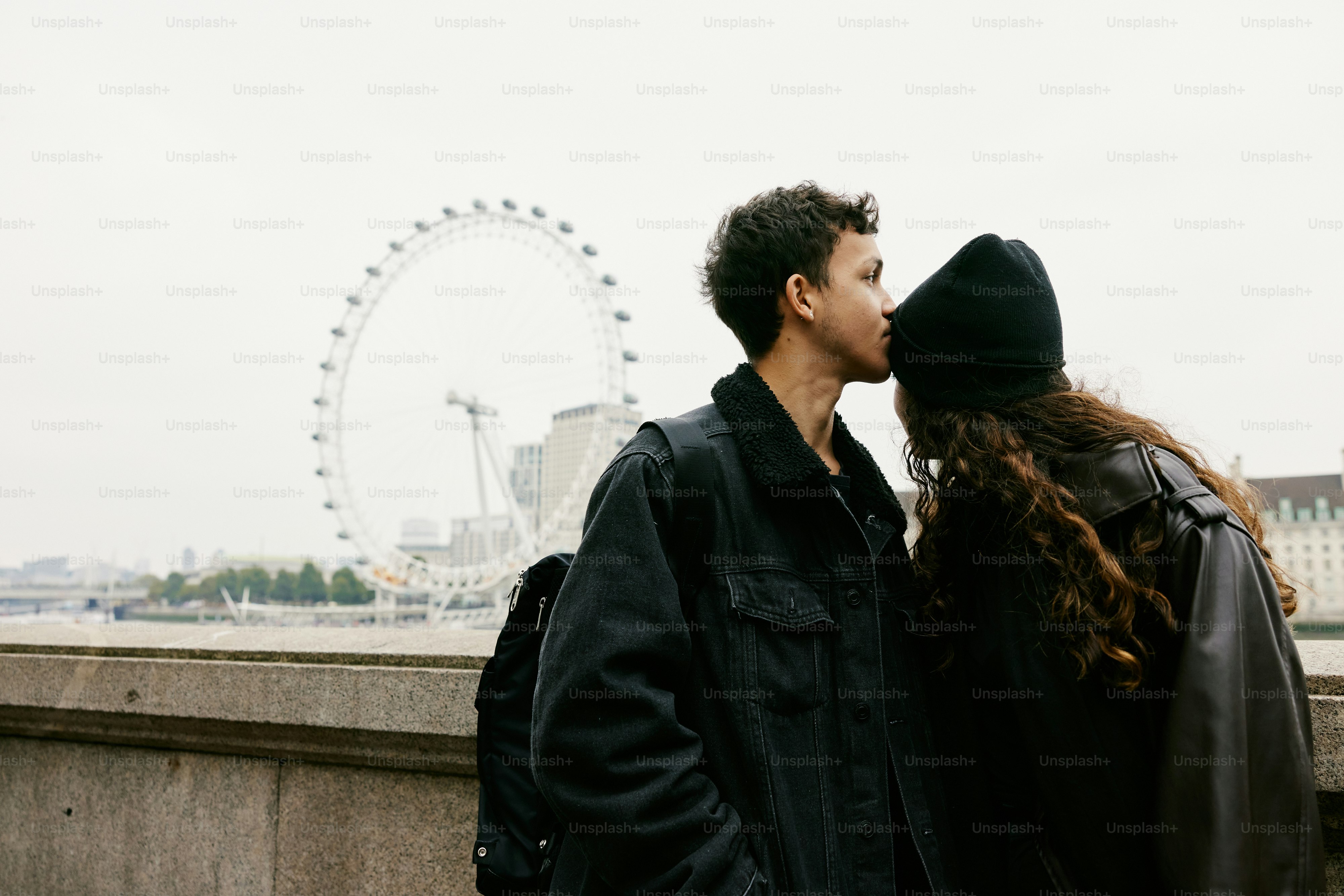 A man and a woman kissing in front of a ferris wheel