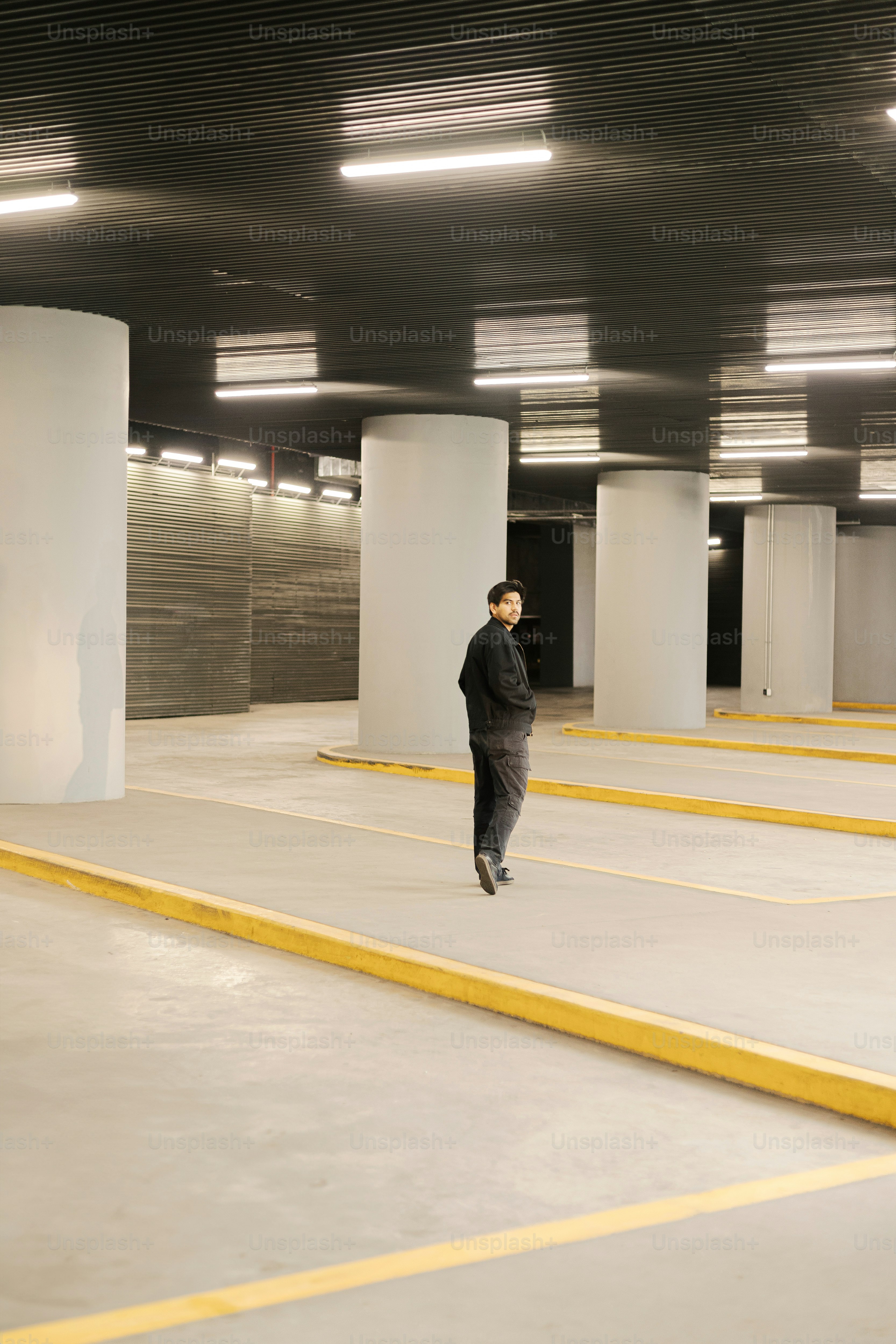 A man walking through a parking garage filled with lots of white pillars